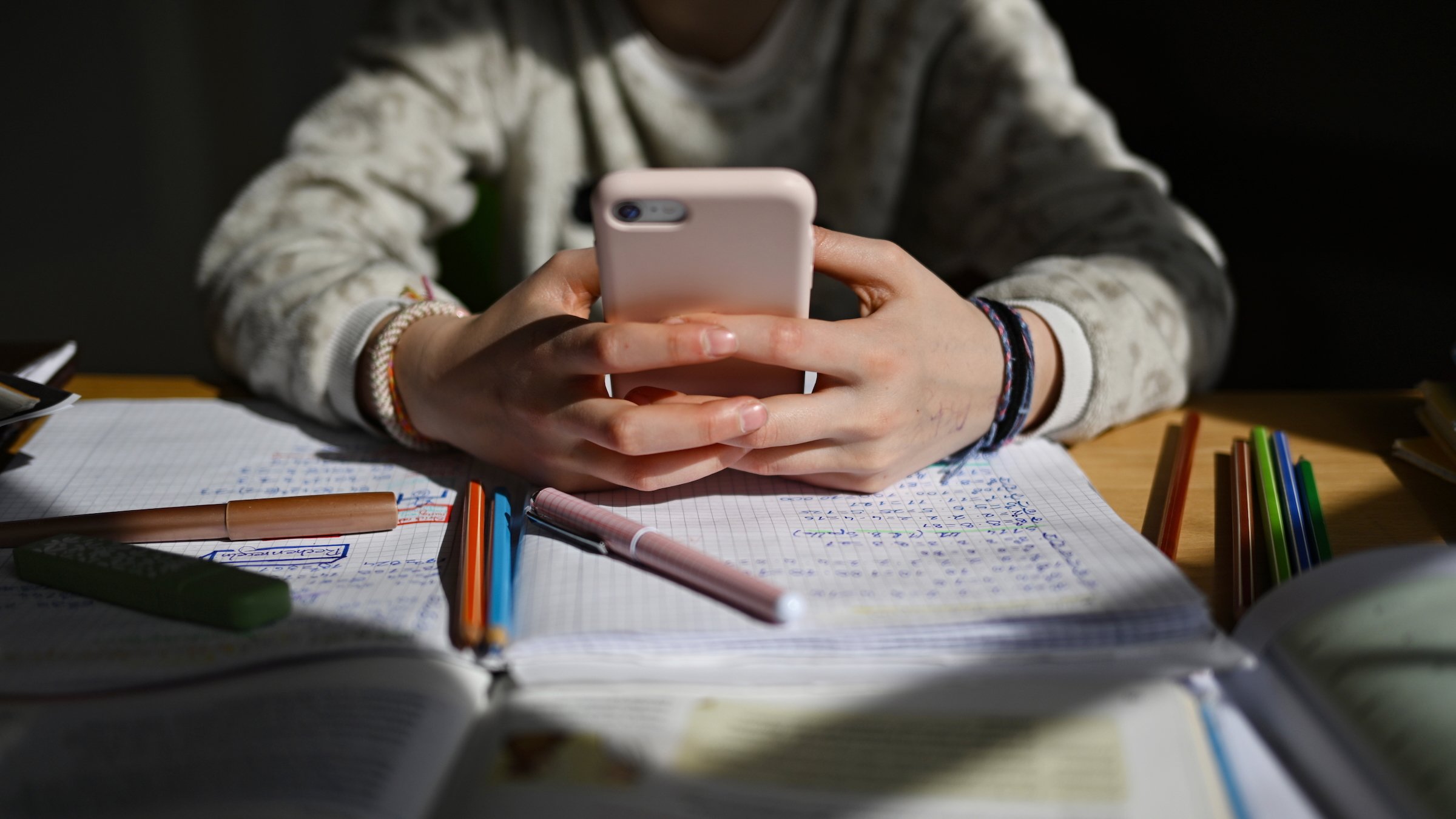 a young person holds a smartphone on their school desk