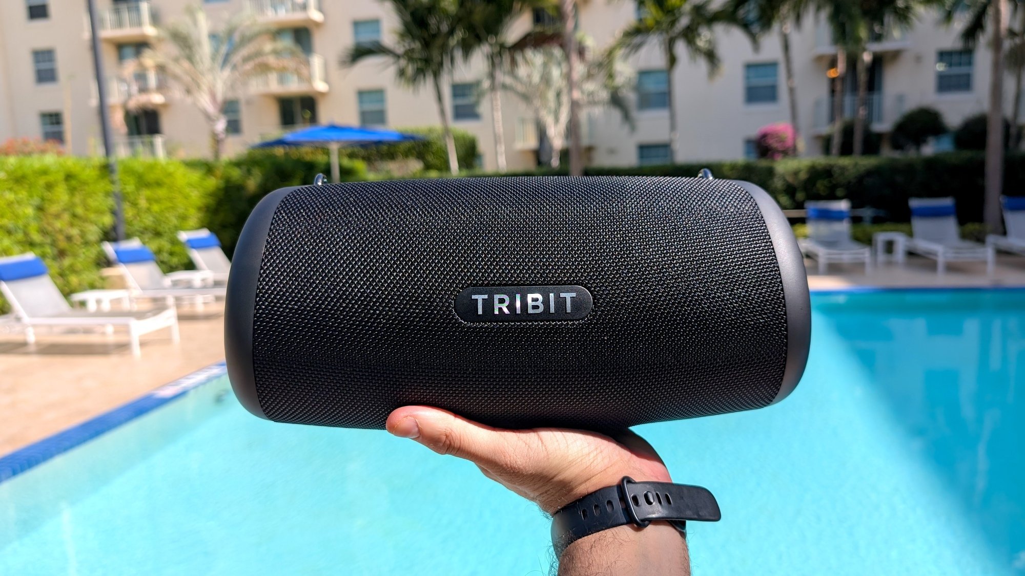man's hand holding the Tribit StormBox Lava speaker up in front of a pool
