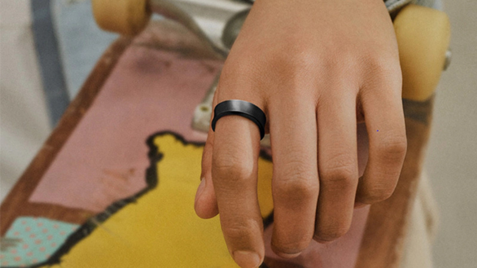 close up of hand wearing black Samsung Galaxy Ring and holding skateboard