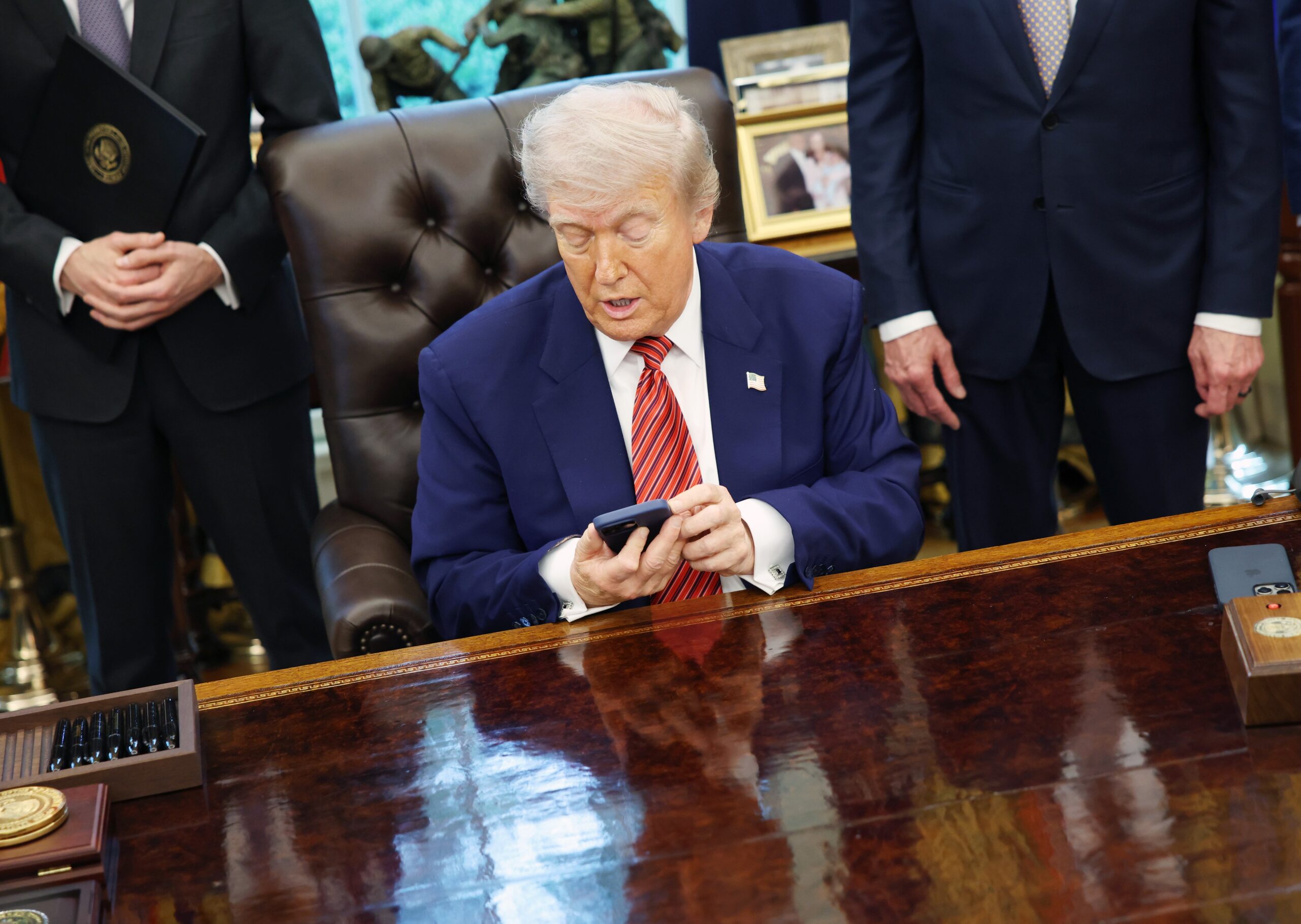 president trump holds an iphone while signing executive order in oval office