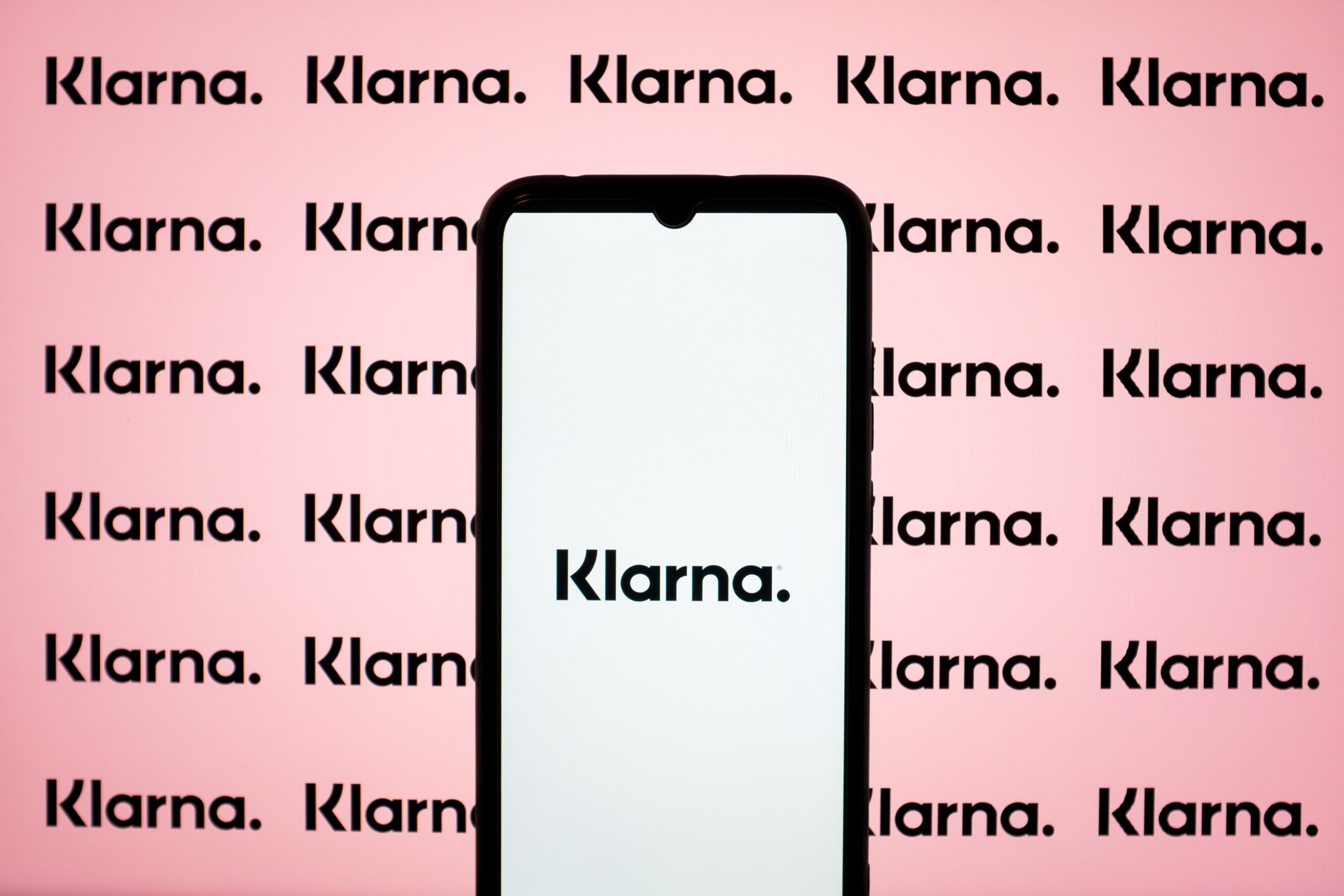 A phone displays the Klarna logo in front of a pink background.