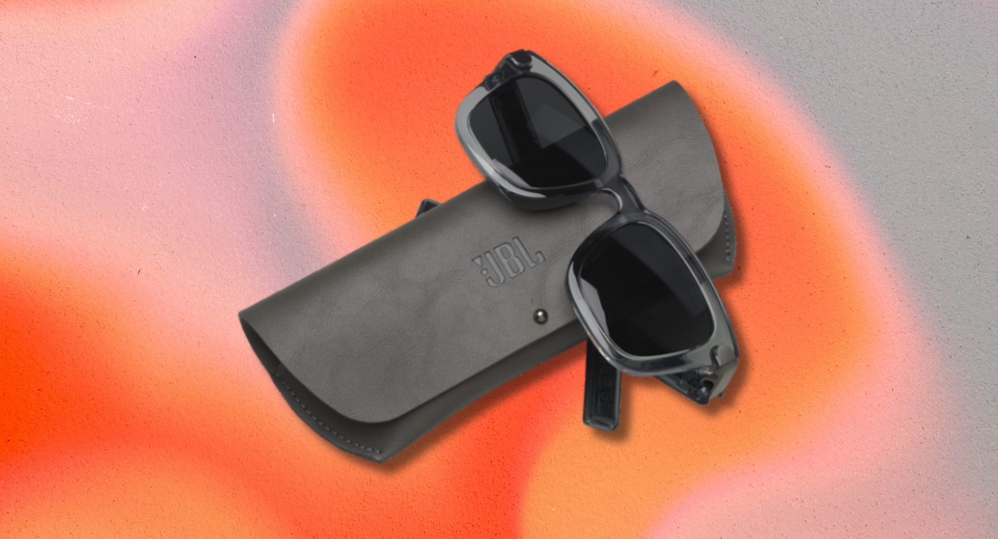 JBL smart audio sunglasses resting on a gray branded case against a textured backdrop of blended orange and pink hues.