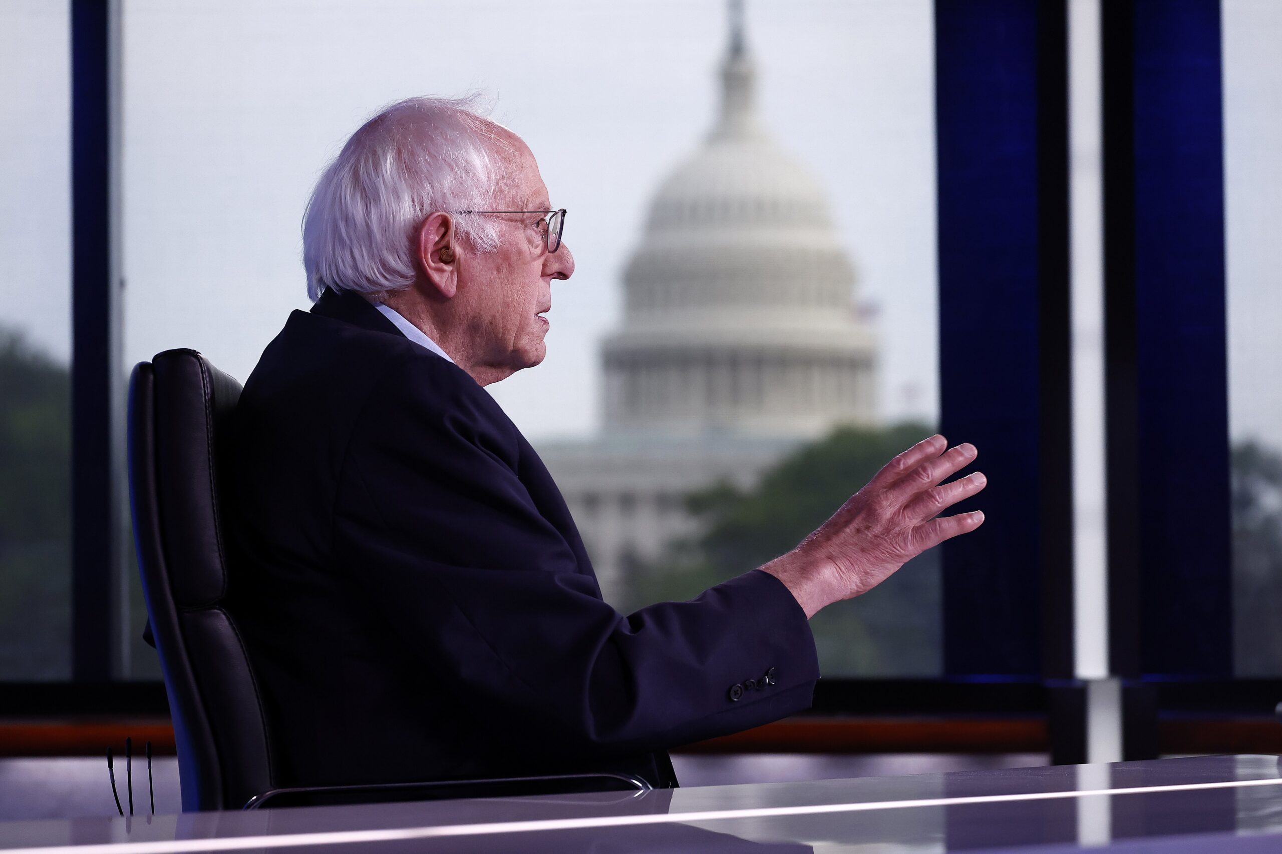bernie sanders sitting at a desk with the capitol building in the background