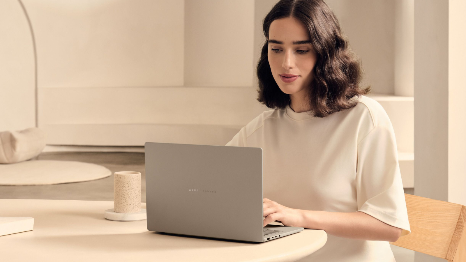 a woman typing on an asus zenbook a14 in a beige room