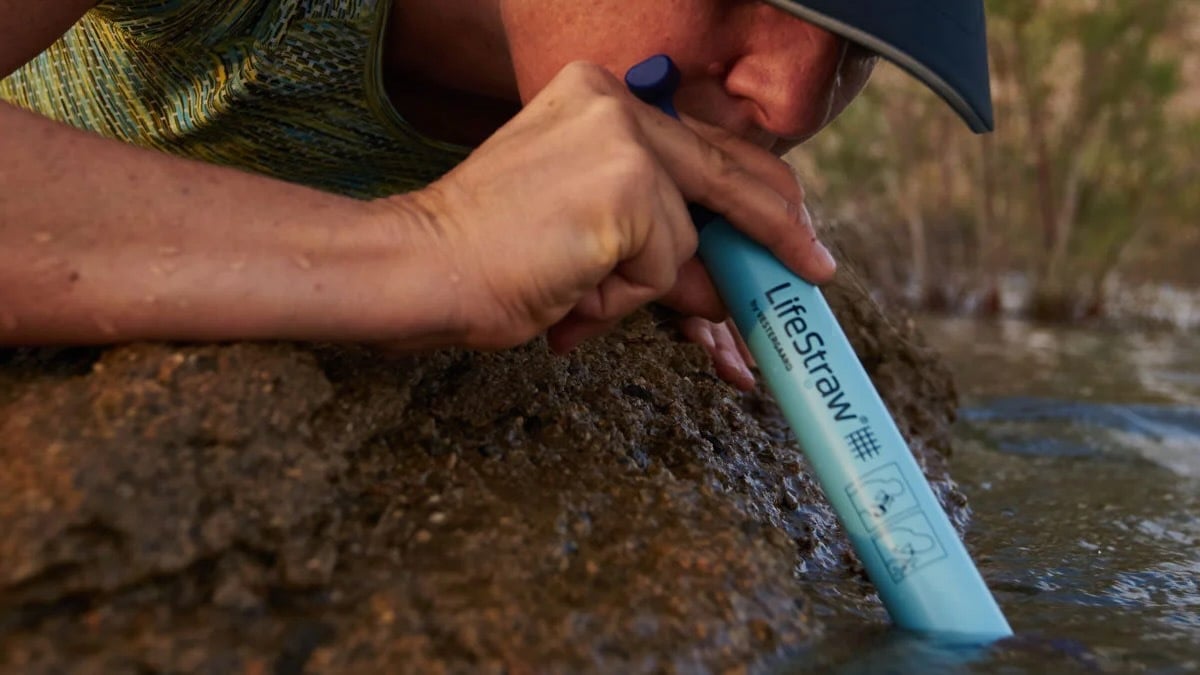 woman sipping from lifestraw inserted in river