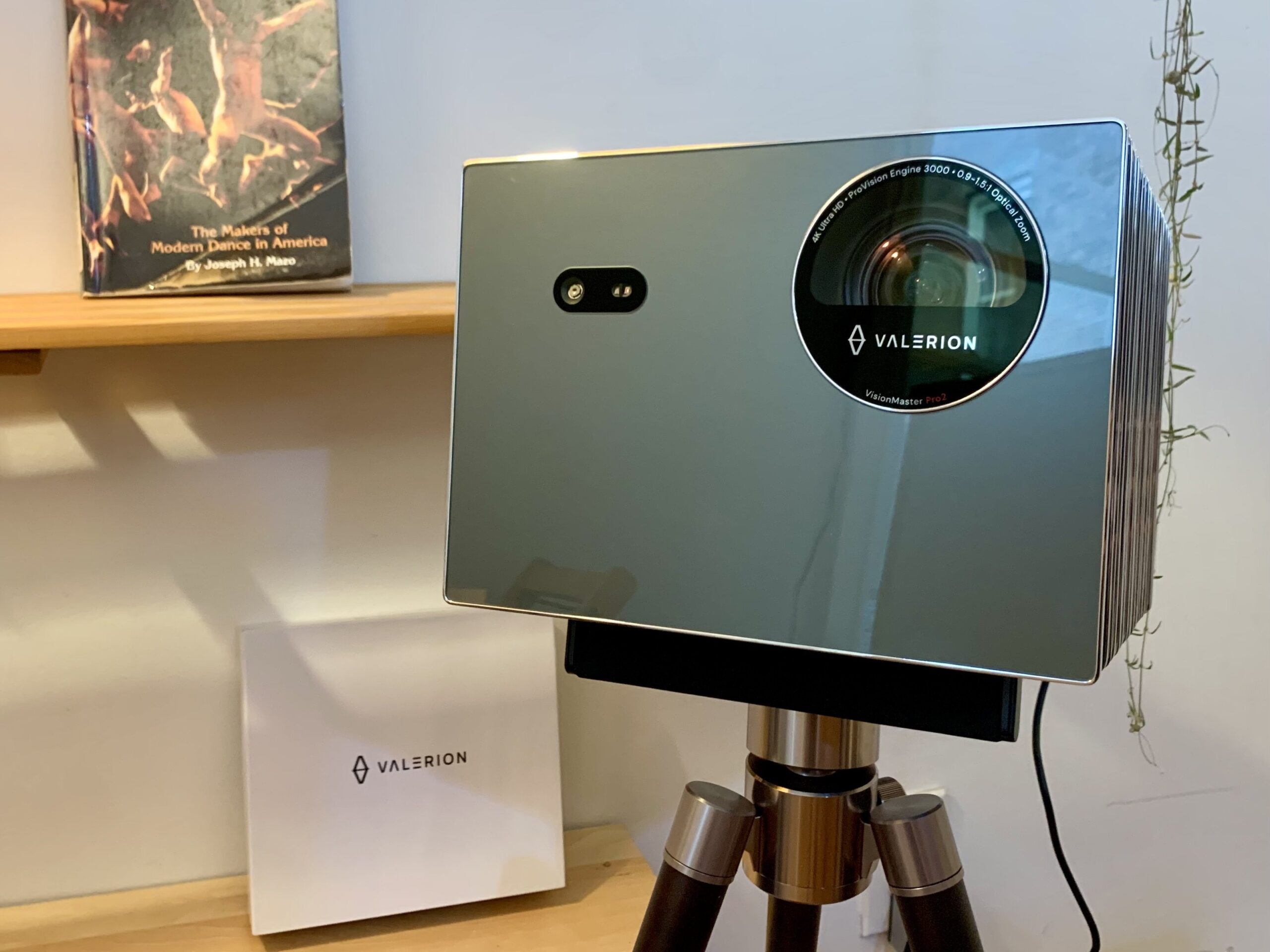 The Valerion VisionMaster Pro 2 projector appears in a room next to a shelf and a plant.