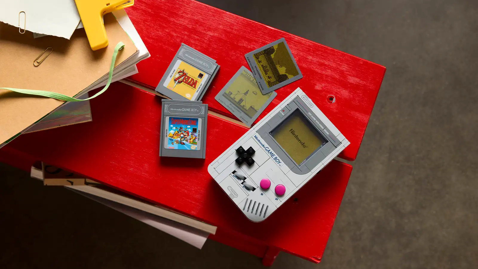 a flat lay of the lego game boy next to its accessories on a red surface