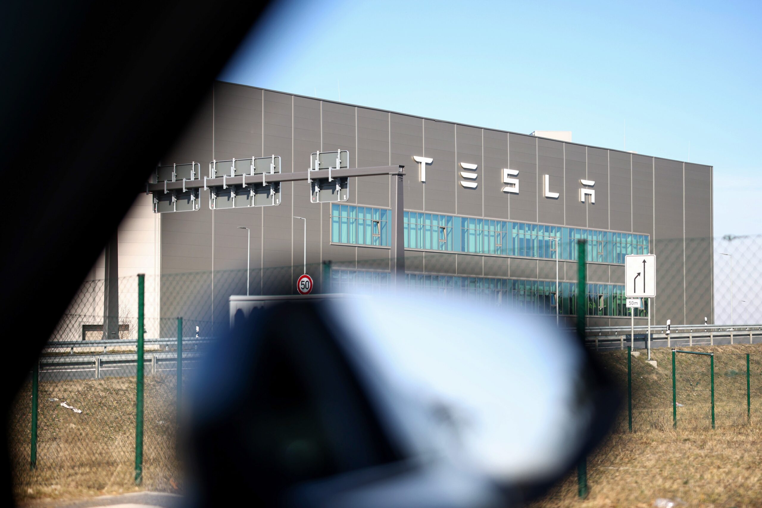A photo of the outside of a Tesla factory framed through the window of a car. 