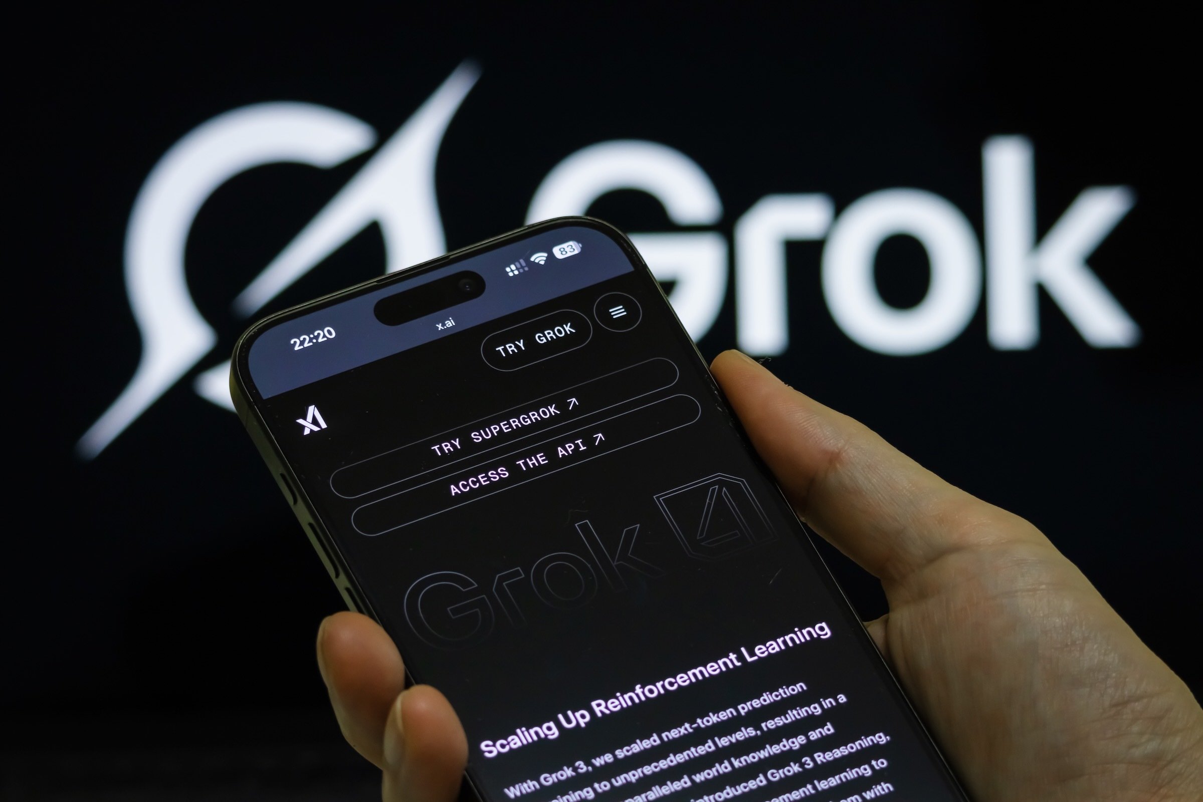 person holds iphone with grok 4 on display and grok logo in background
