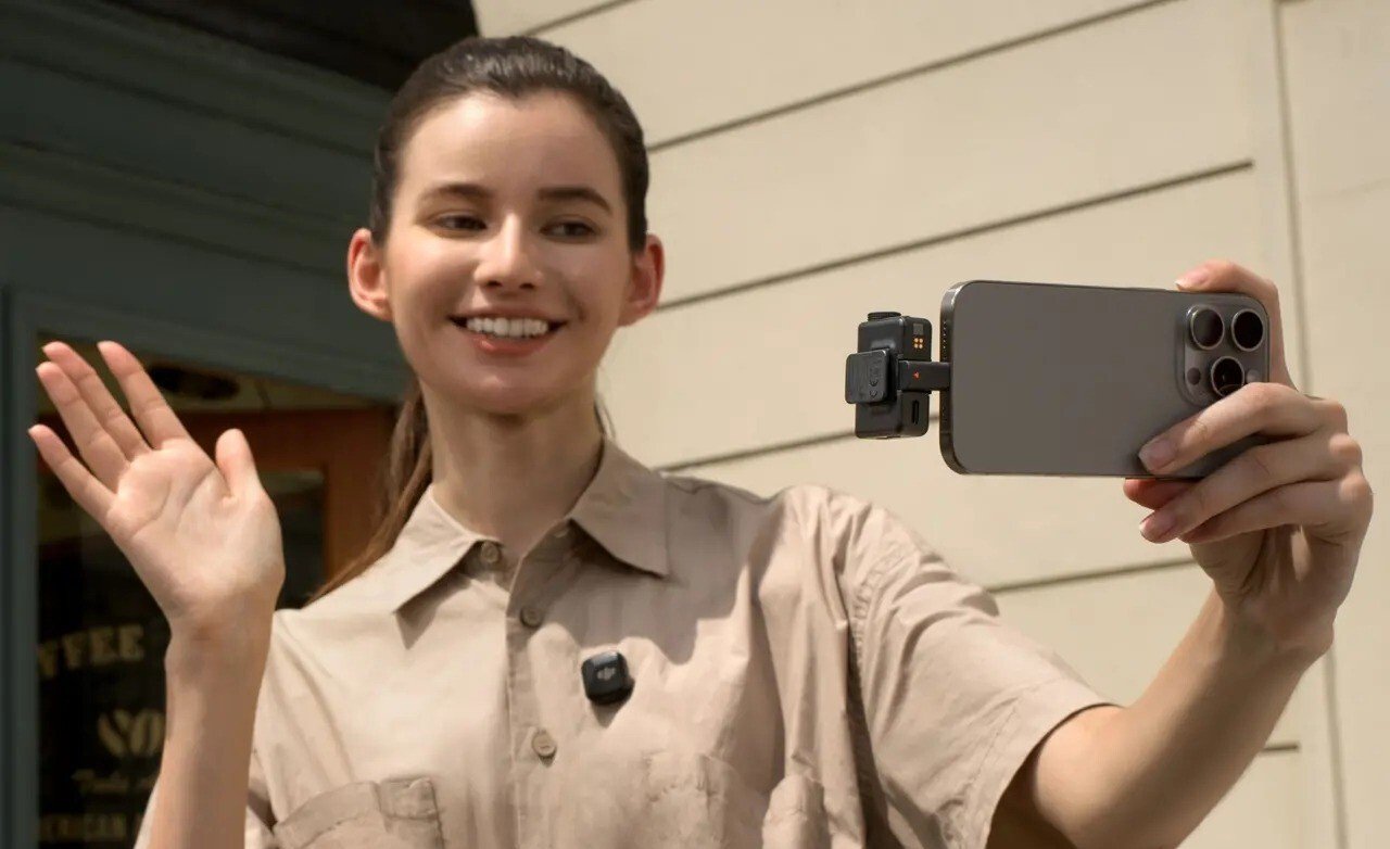 a person wears the DJI Mic Mini while holding a phone in the left hand and waving to the camera