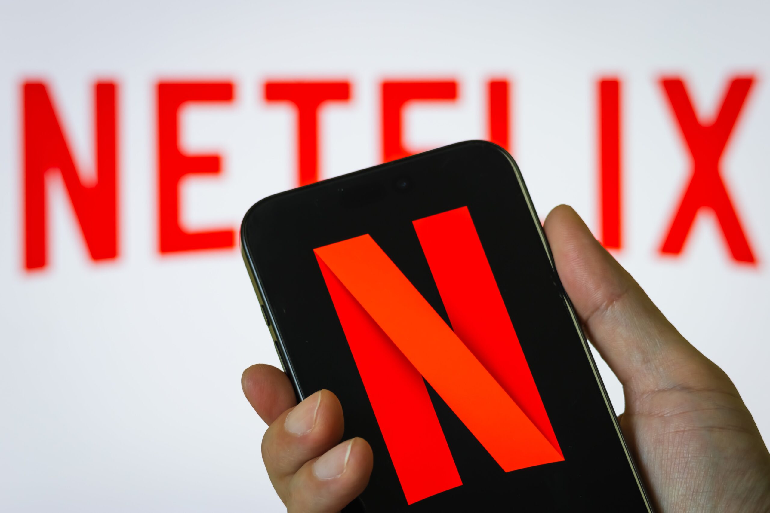 a person holds a smartphone in vertical orientation displaying the red N logo of Netflix
