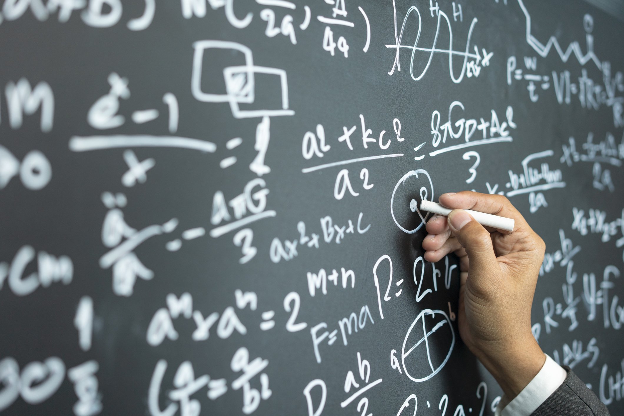 hand writing a complex math problem on a chalkboard 