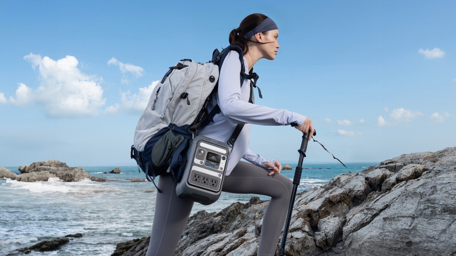 a person wears the anker solix c300 with a shoulder strap while walking over rocky terrain on a beach 