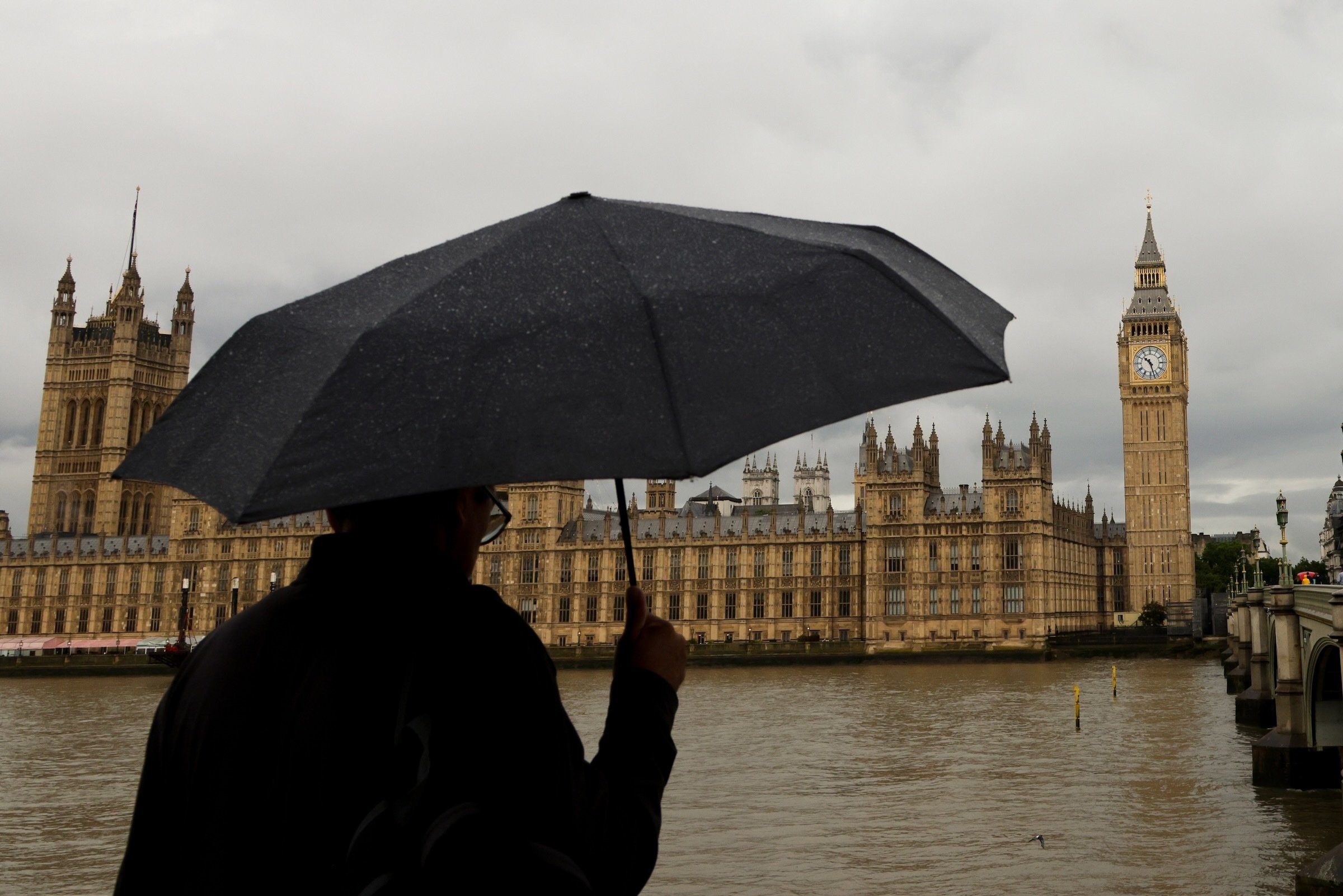 A man under an umbrella looks at the Houses of Parliament and Big Ben in Westminster, London