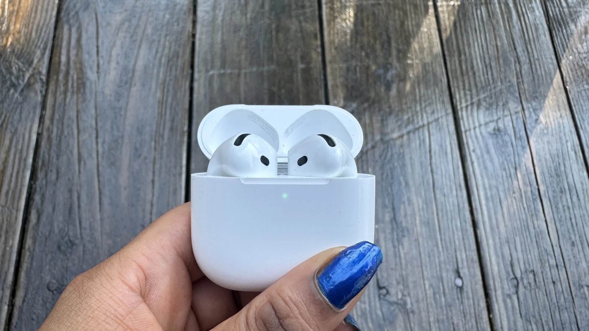 hand holding Apple AirPods 4 with wooden deck in background
