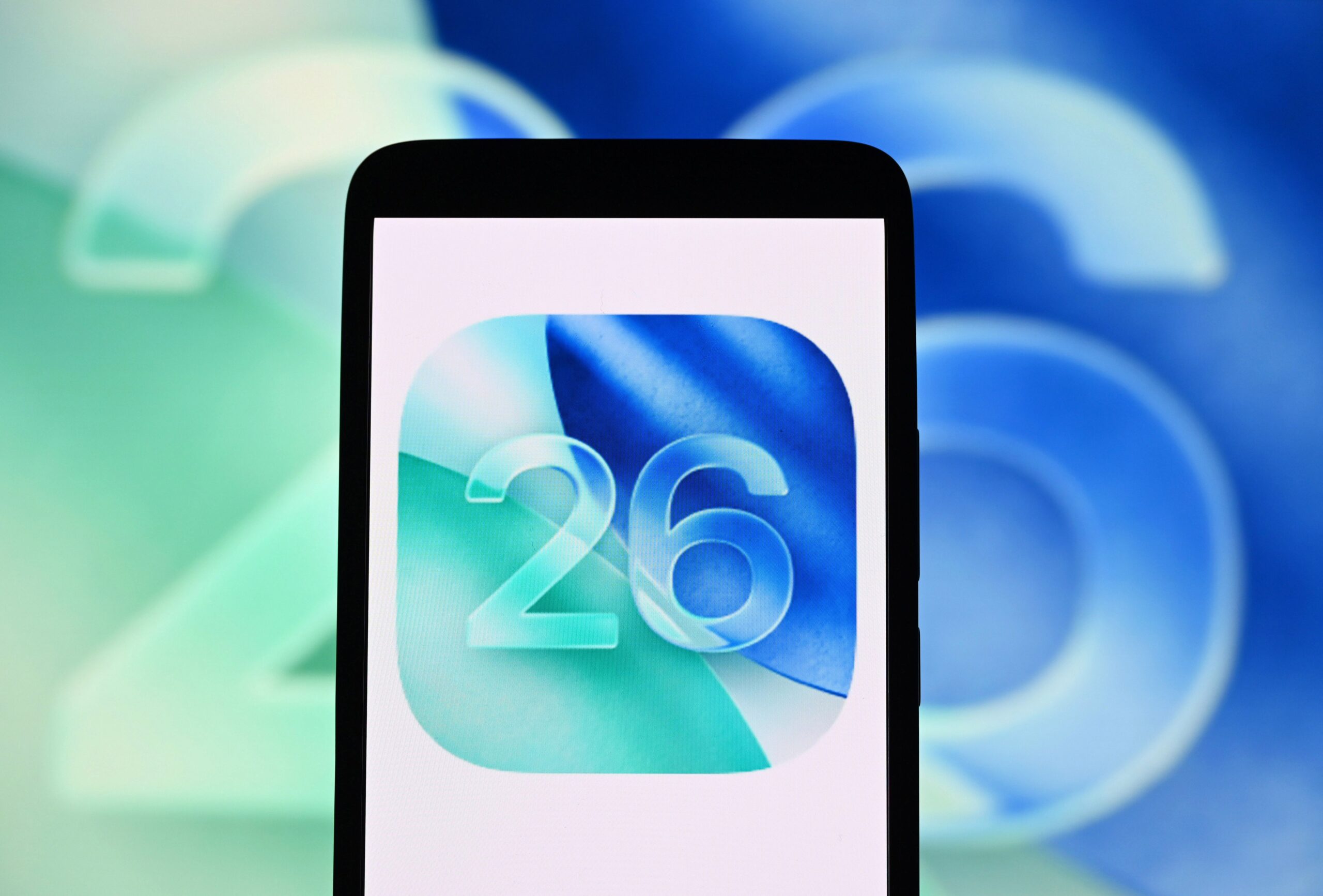 The iOS 26 logo is seen on a smartphone and in the background.