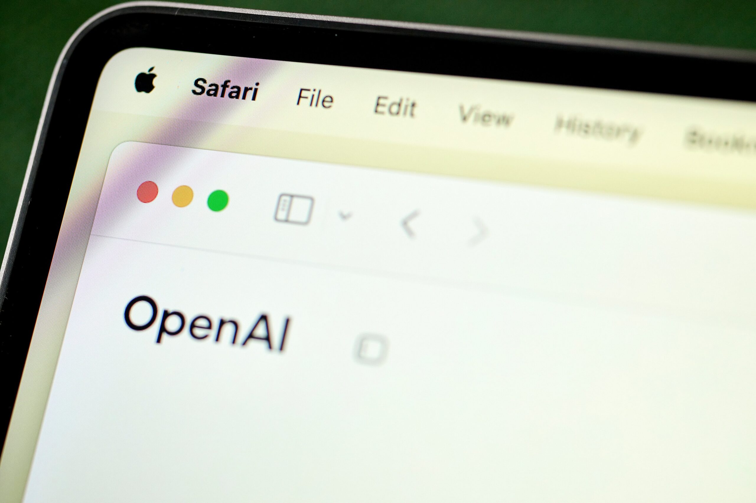 A laptop screen shows the edge of a Safari browser set to the OpenAI homepage