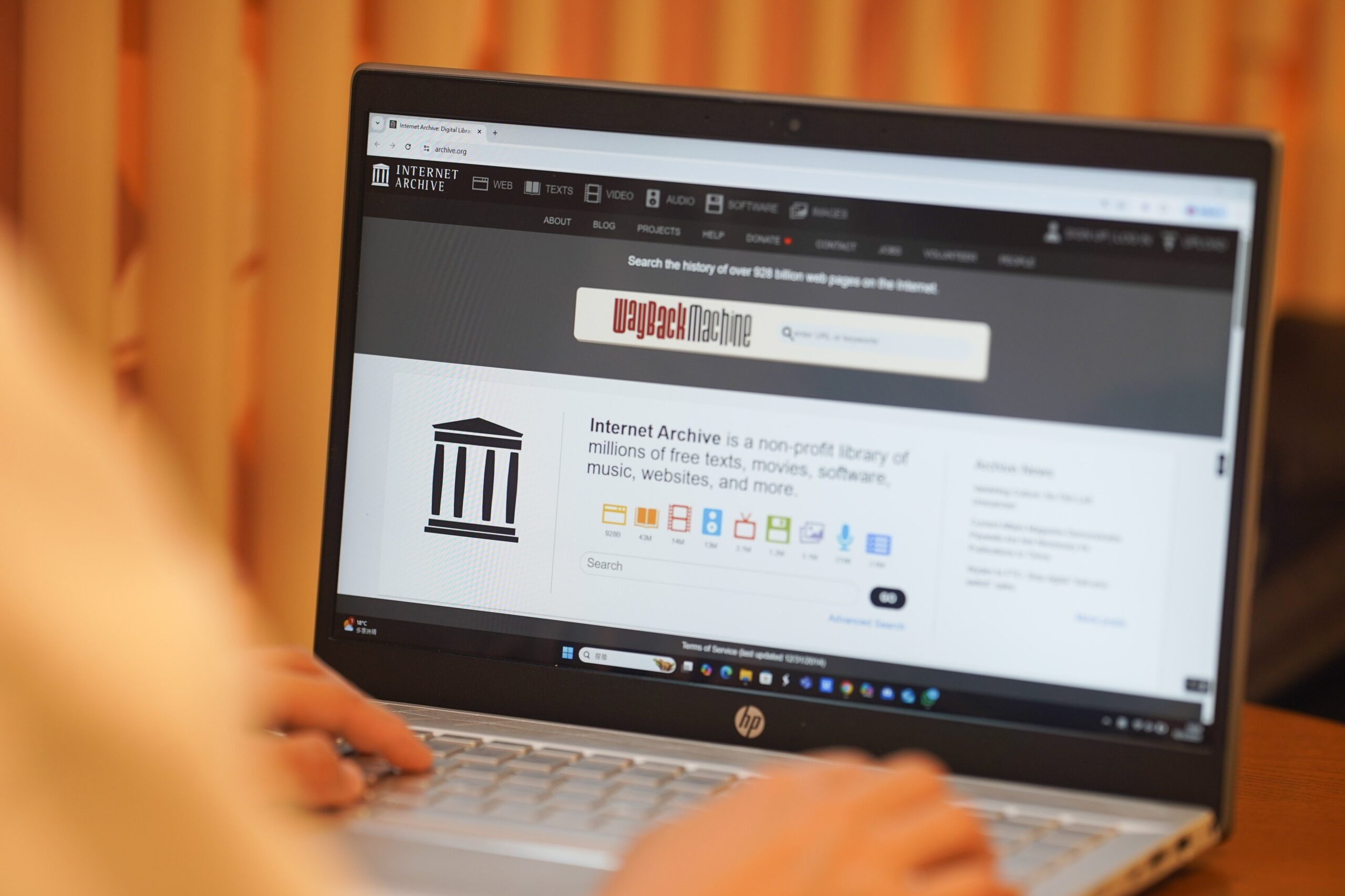 A person typing on a laptop. The laptop screen is open to the Internet Archive website. 