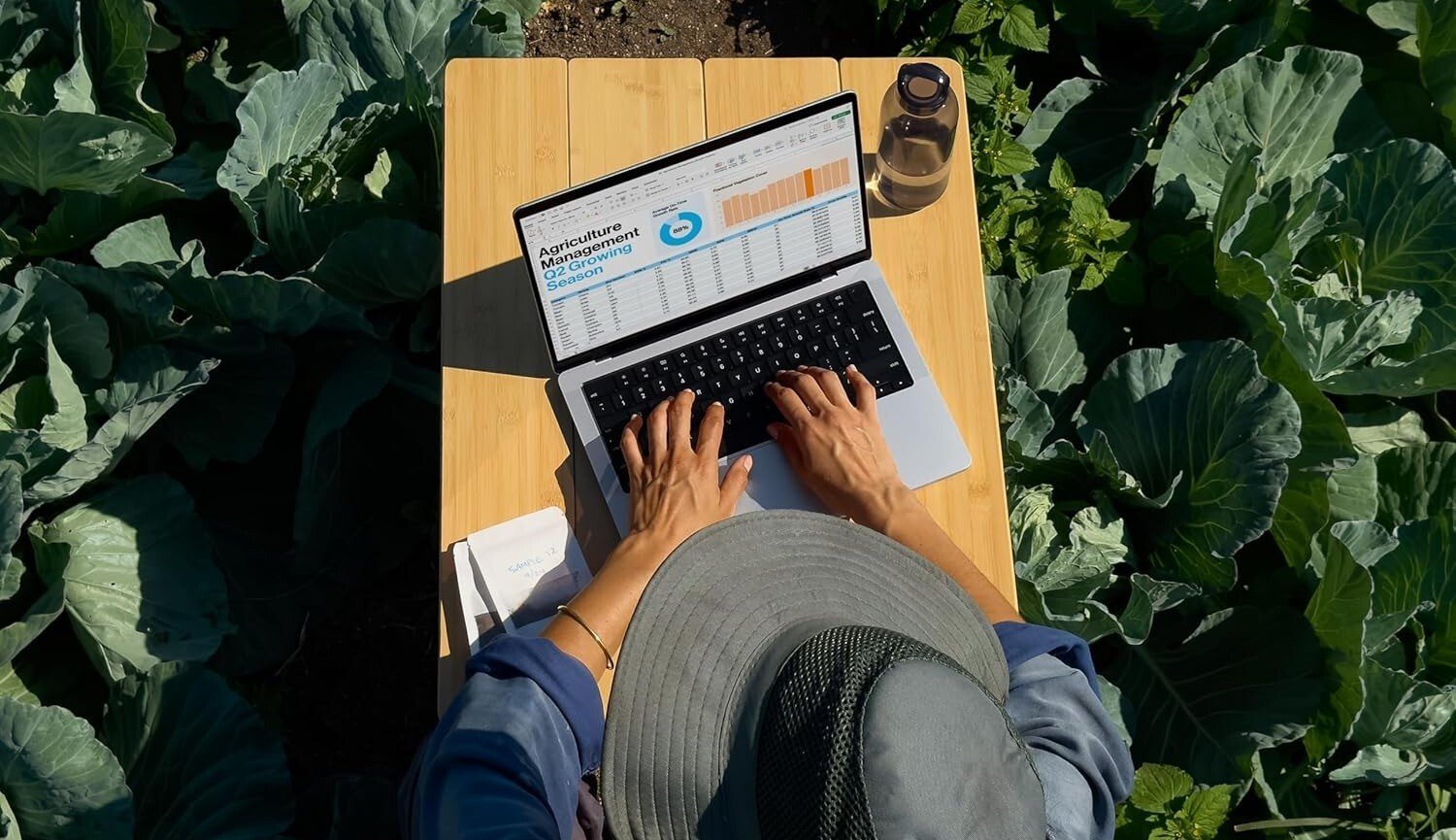 a person in a farming field uses the MacBook Pro laptop, as seen from an aerial view
