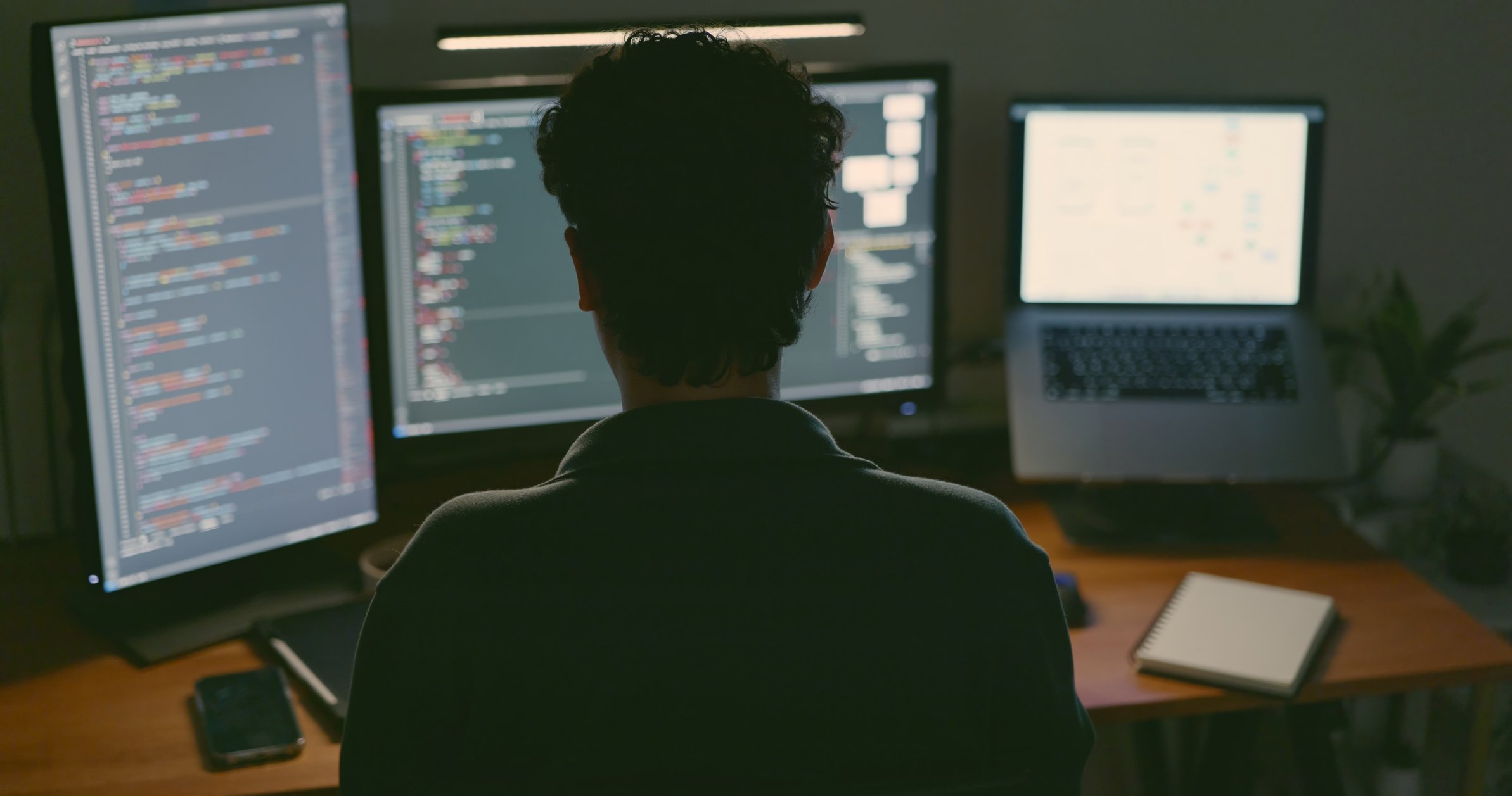back of engineer's head sitting at multiple computer monitors