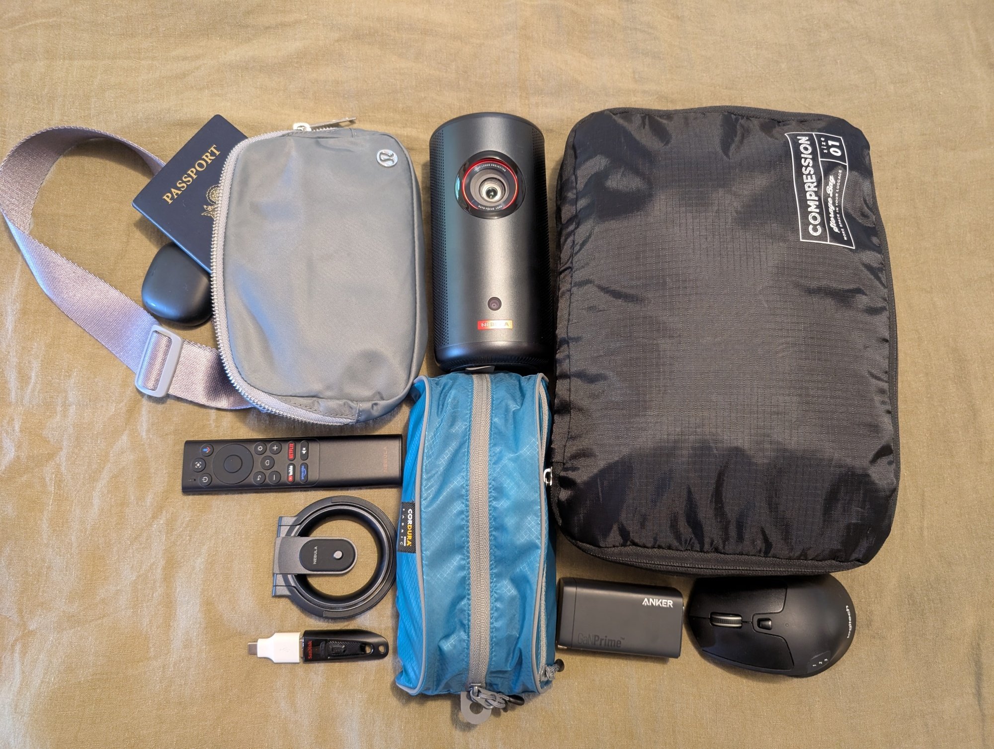 the anker nebula capsule 3 laser projector on a bed with other packing items like a compression bag, a remote control, a sling bag, and a passport.