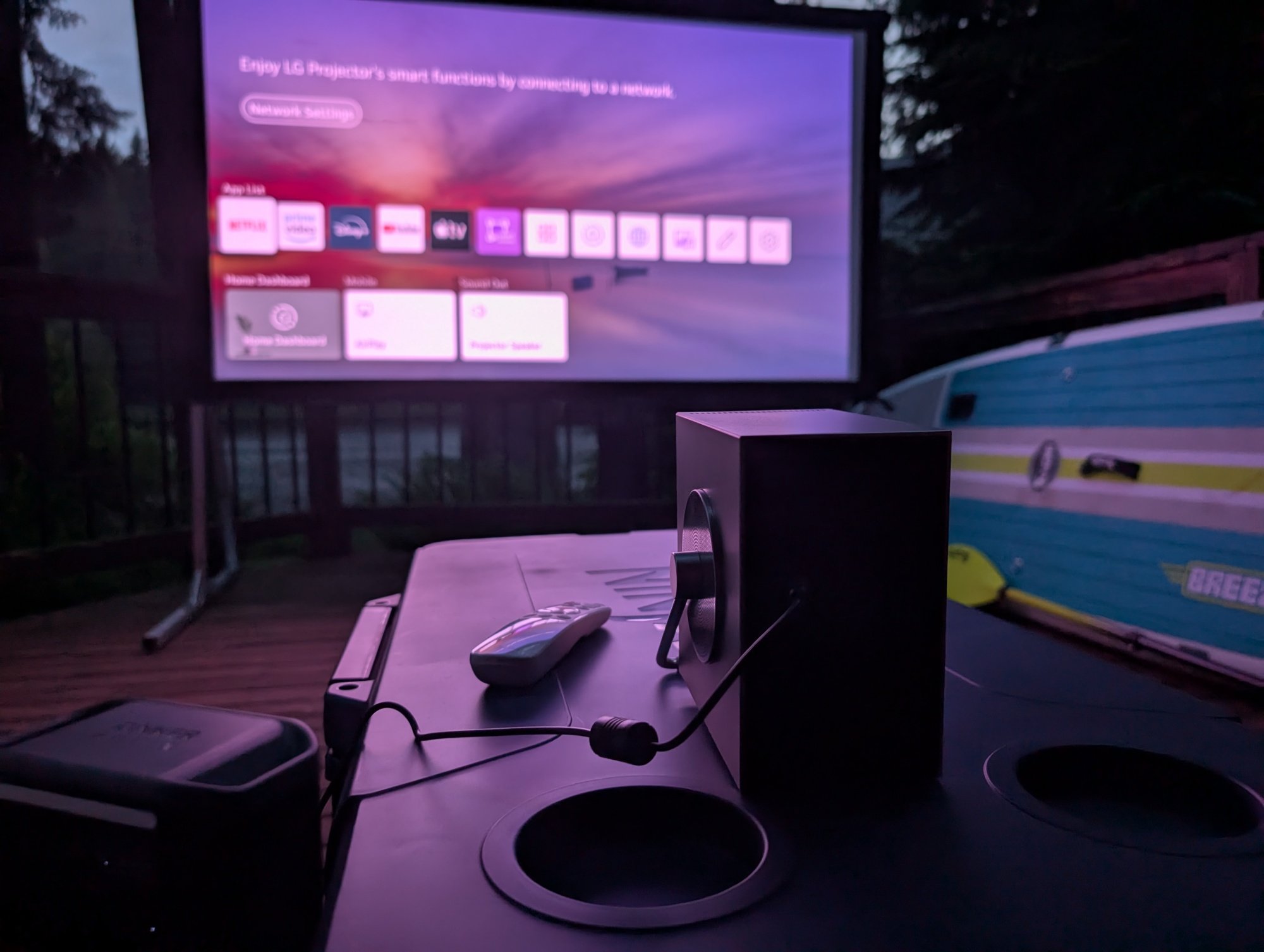 an LG CineBeam Q 4K projector sits on a cooler, displaying the LG webOS menu on a projector screen