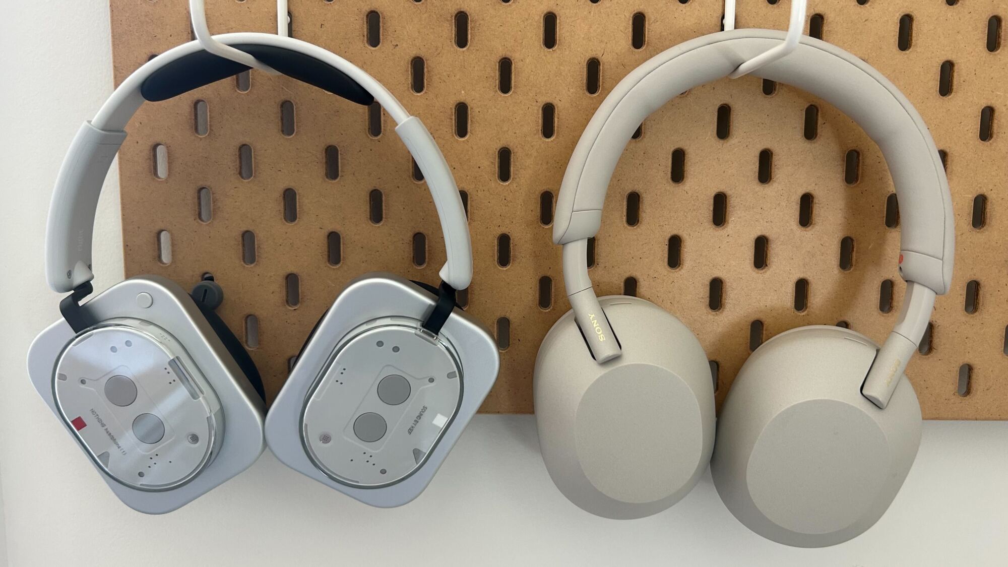 white nothing headphones hanging on pegboard hook next to silver sony wh-1000xm5 headphones
