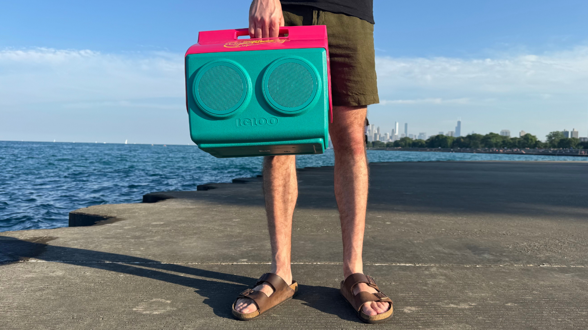 a close-up of a man holding an igloo kooltunes speaker on concrete steps near a lake