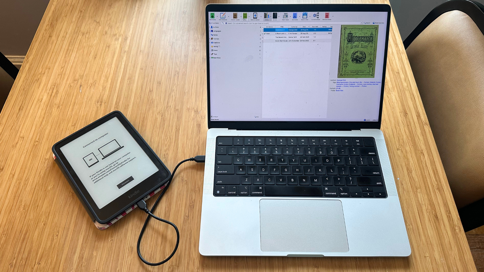 A laptop on a wooden table with a Kindle plugged into it