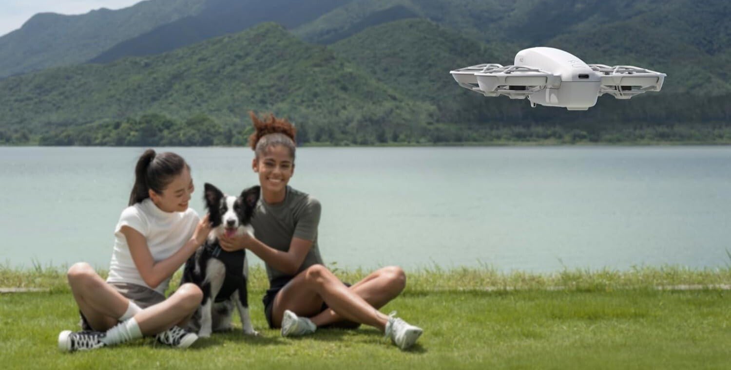 the dji neo drone in flight in front of two people posing with a dog in between them.