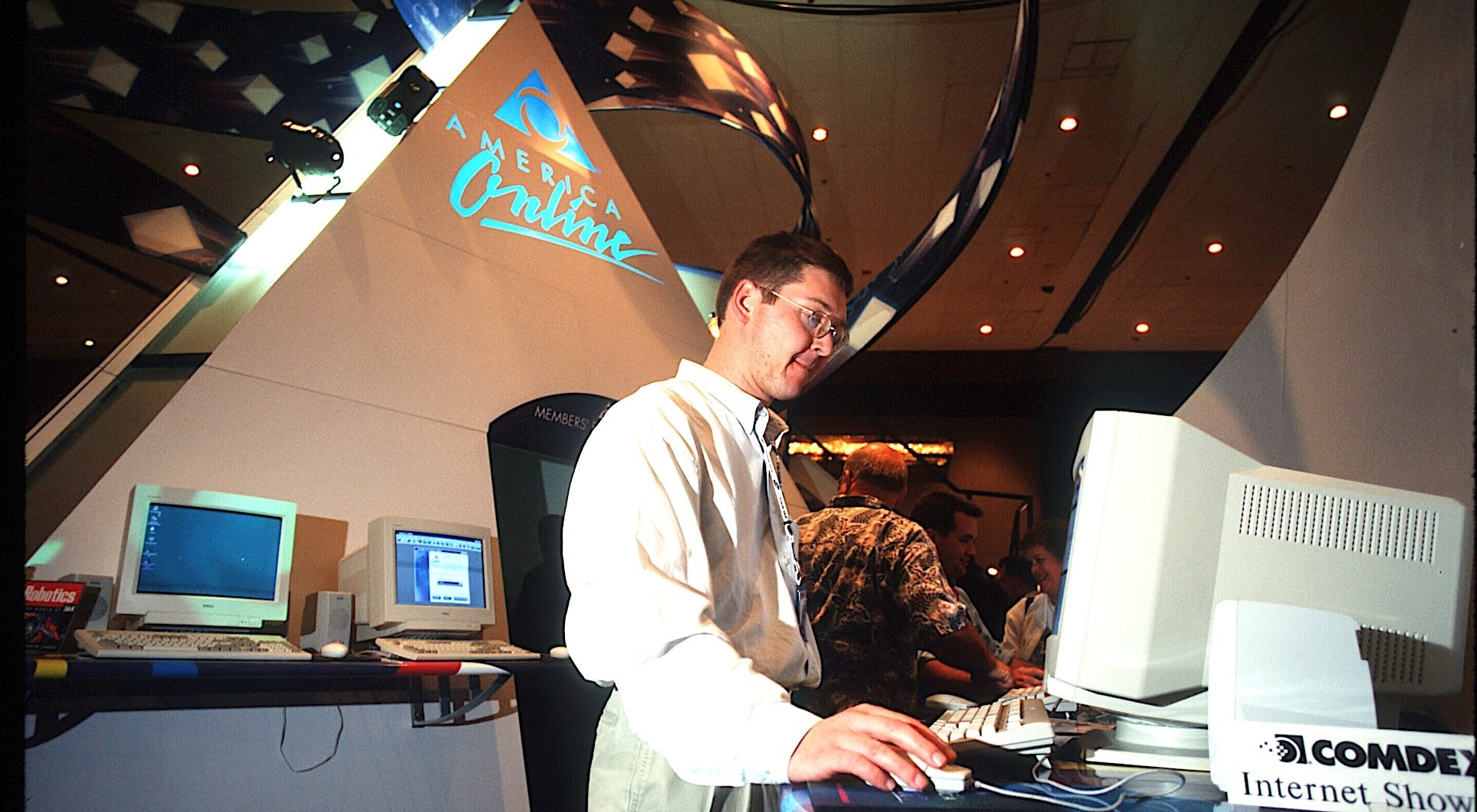 Under a giant AOL logo, a man looks at a 1990s computer.