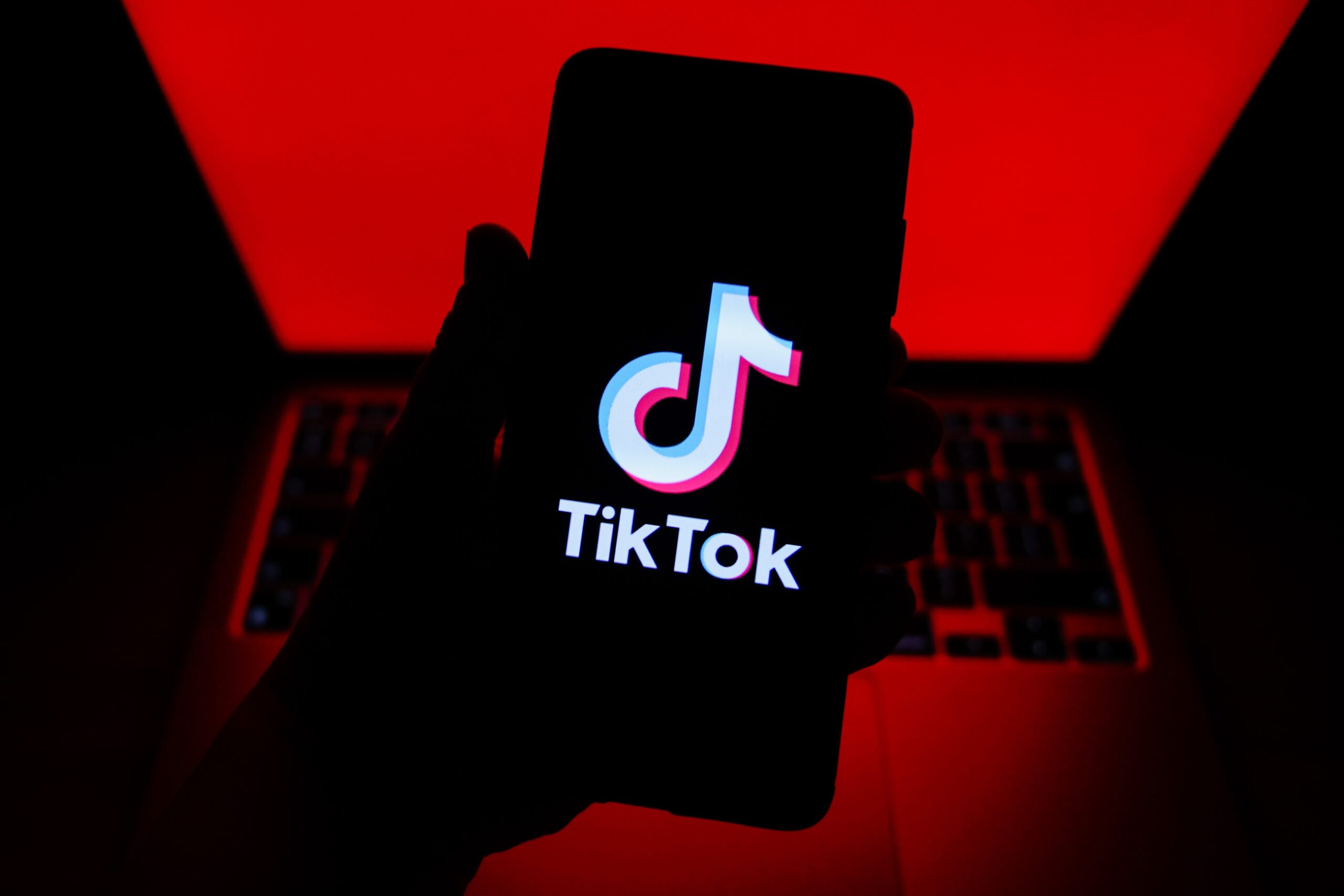 tiktok logo on a phone in front of red computer screen