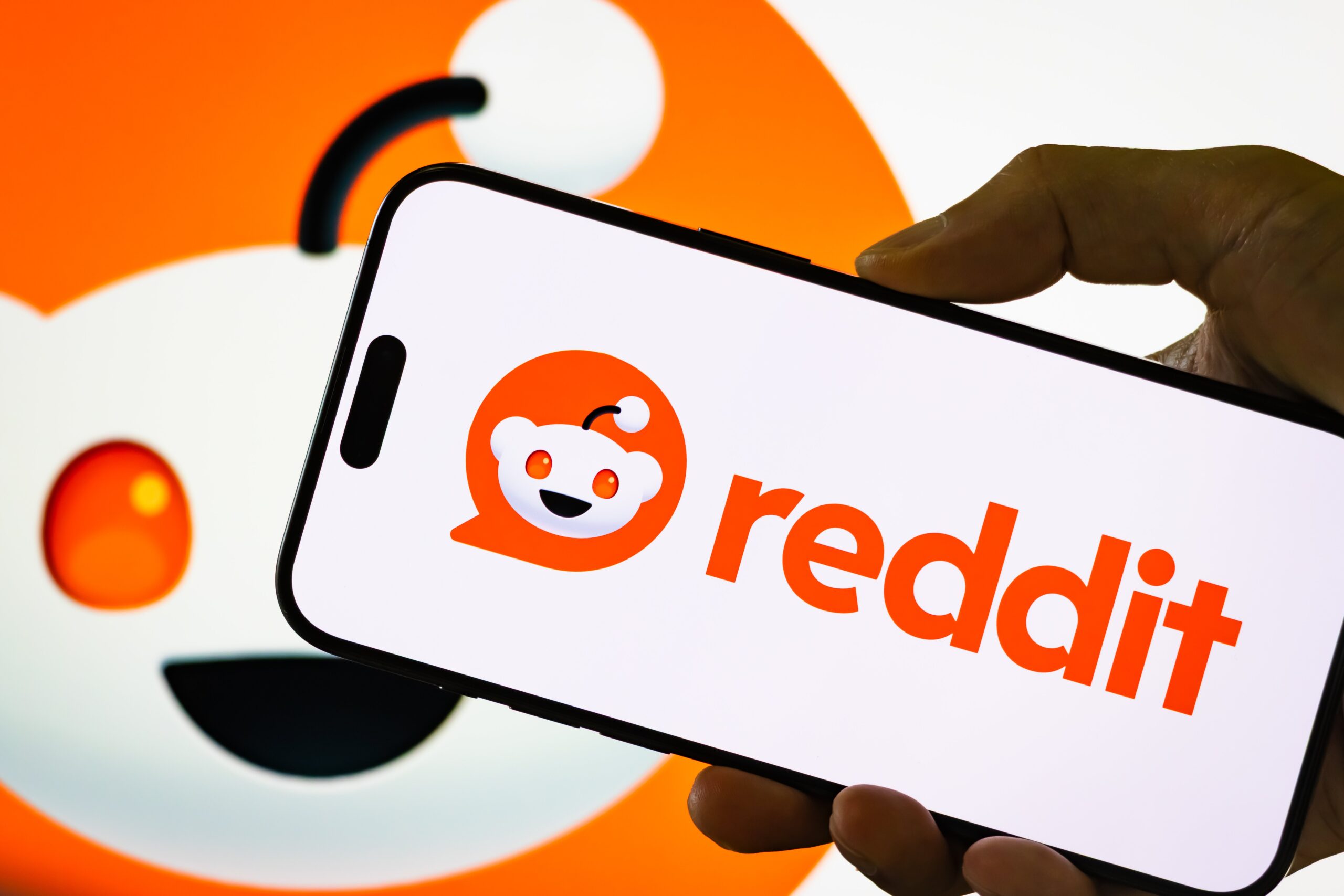 A person holds a smartphone displaying the logo of Reddit Inc