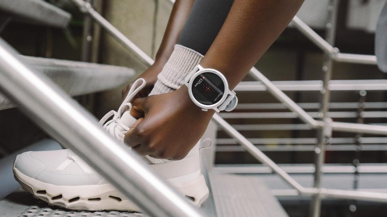 the Nothing CMF Watch 3 Pro on a runner's wrist while they bend over to tie the laces on a white running shoe