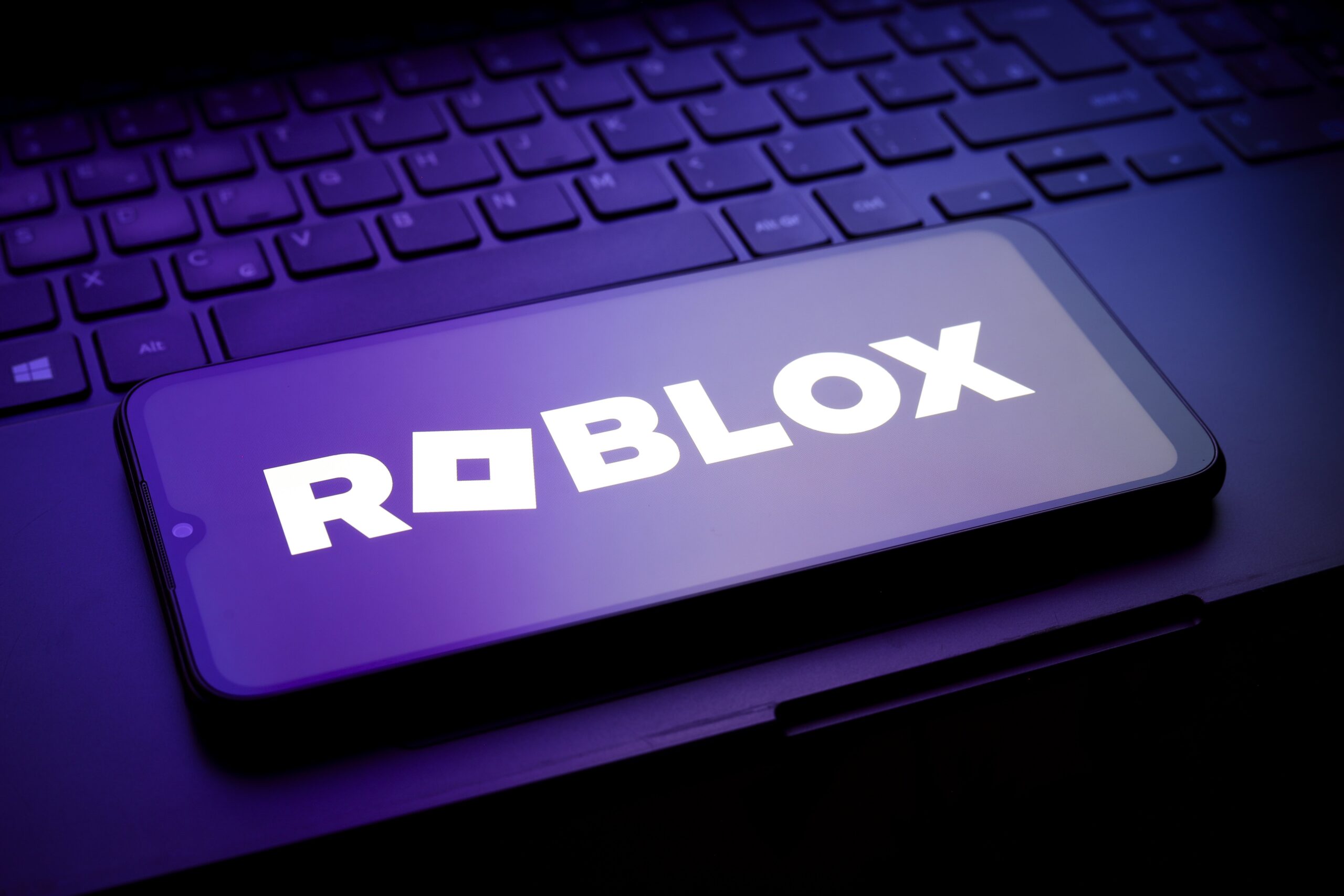 A phone displaying the Roblox logo in dark moody lighting.