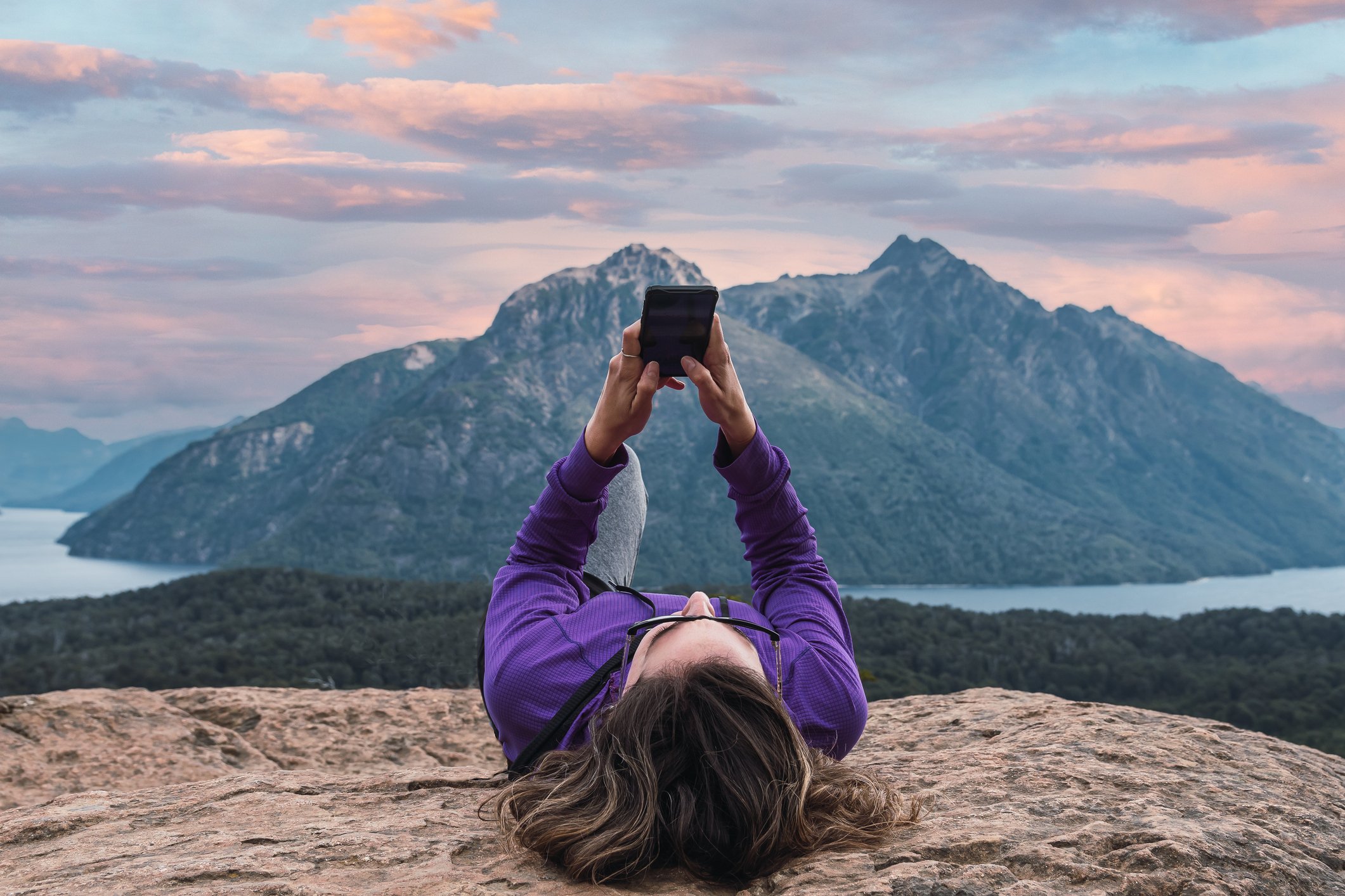 woman lying on the ground overlooking a mountain looking at her phone