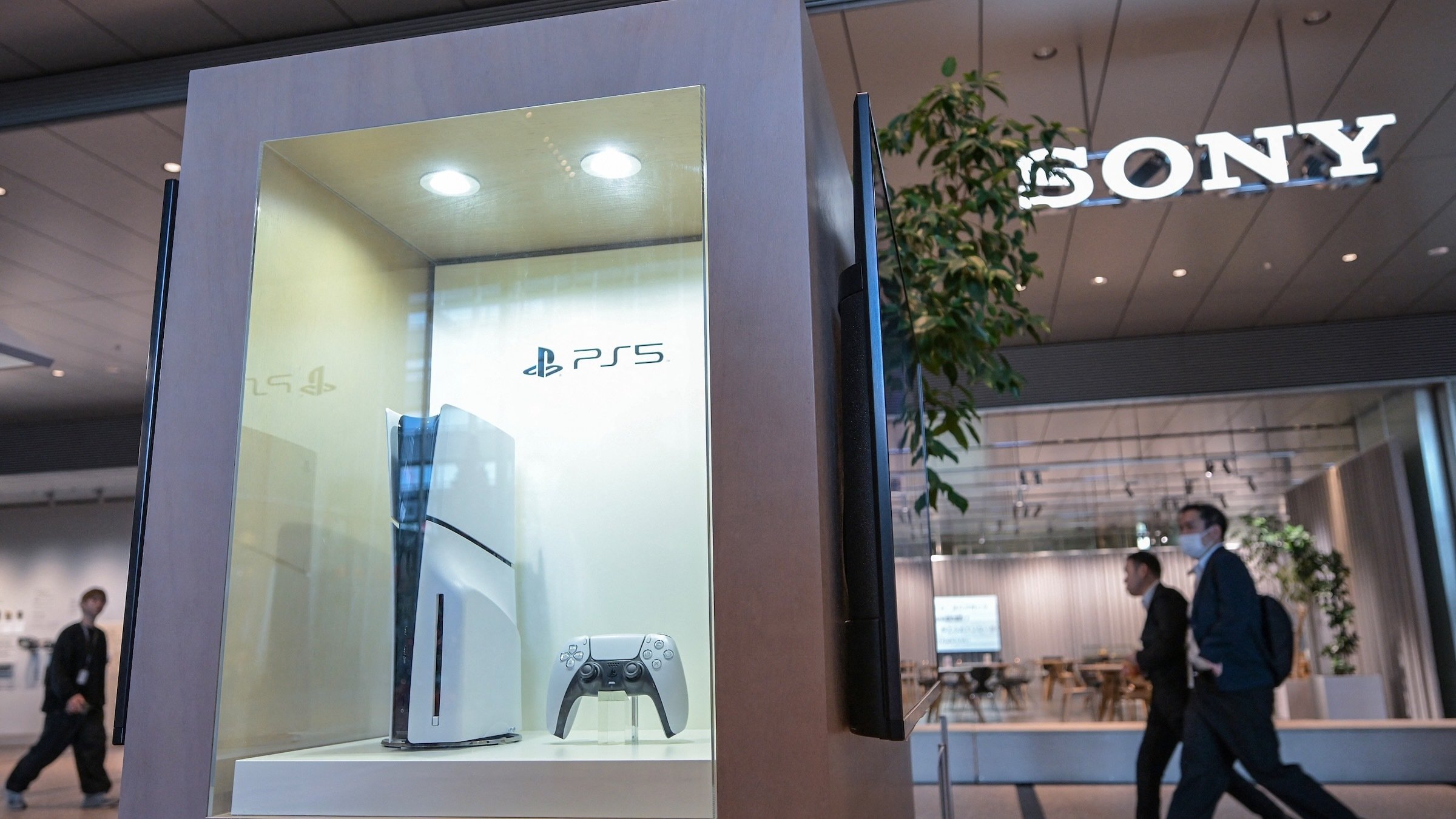 people walk past a ps5 display in front of a sony store