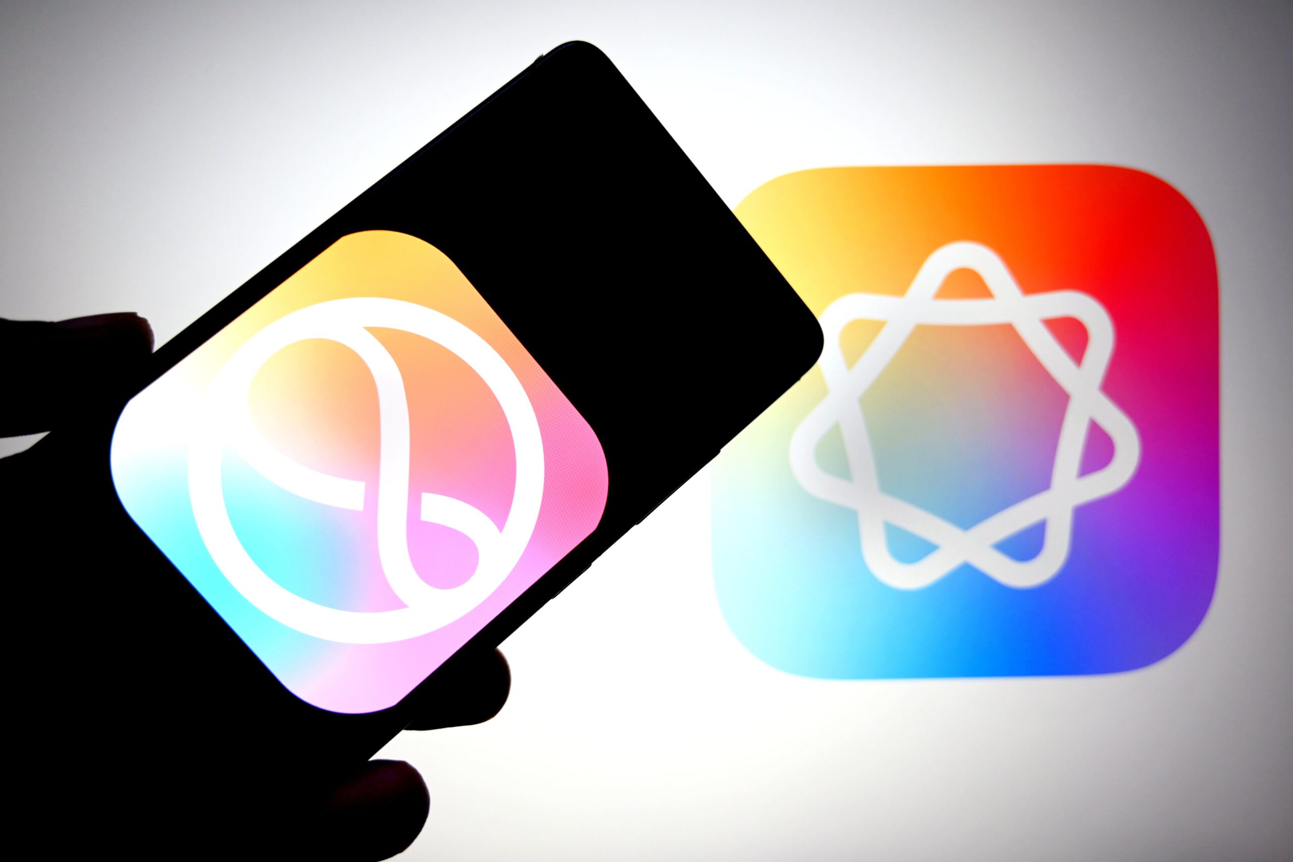 A phone displays the multicolored Siri logo in front of a similarly hued Apple Intelligence logo.