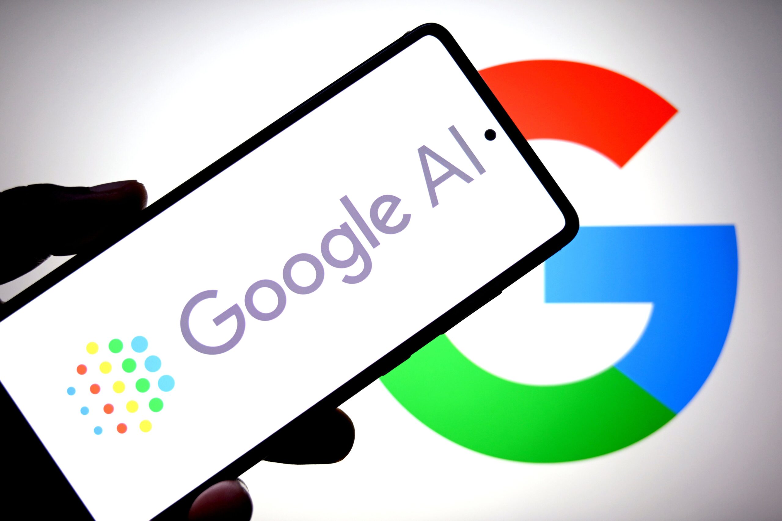 A Google AI logo is seen displayed on a smartphone with a Google logo in the background.