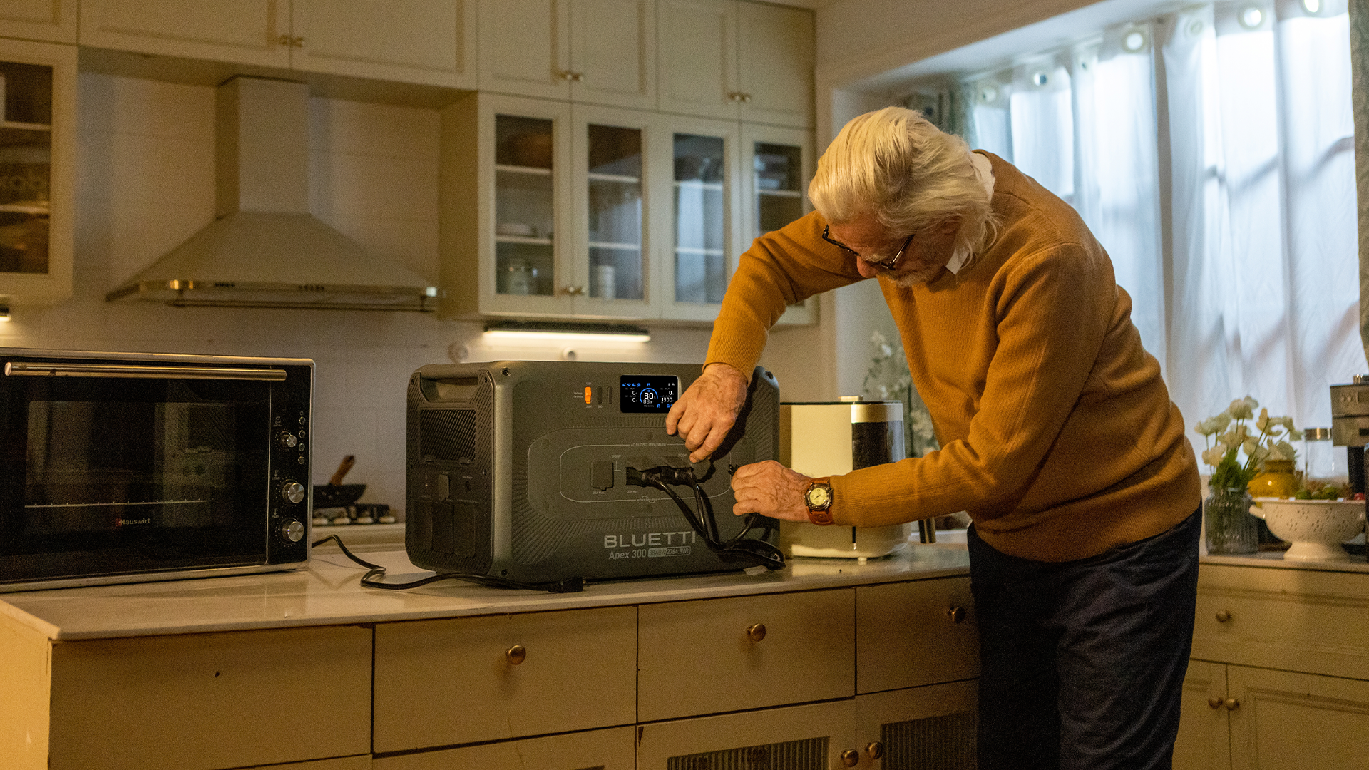 a person plugs something into the Bluetti Apex 300 portable power station while it's sitting inside on a kitchen island.