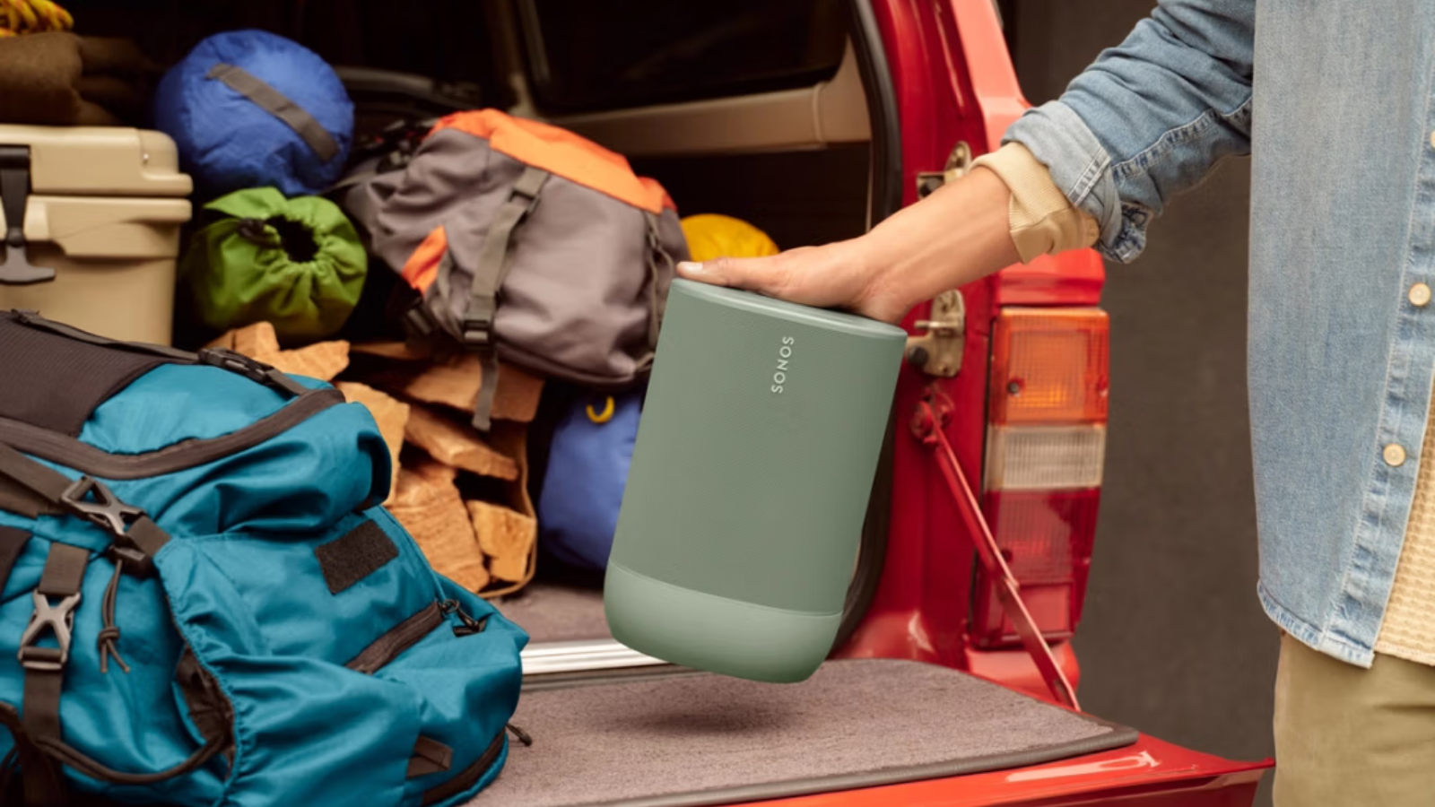 person holding Sonos Move 2 speaker with camping gear in truck tailgate