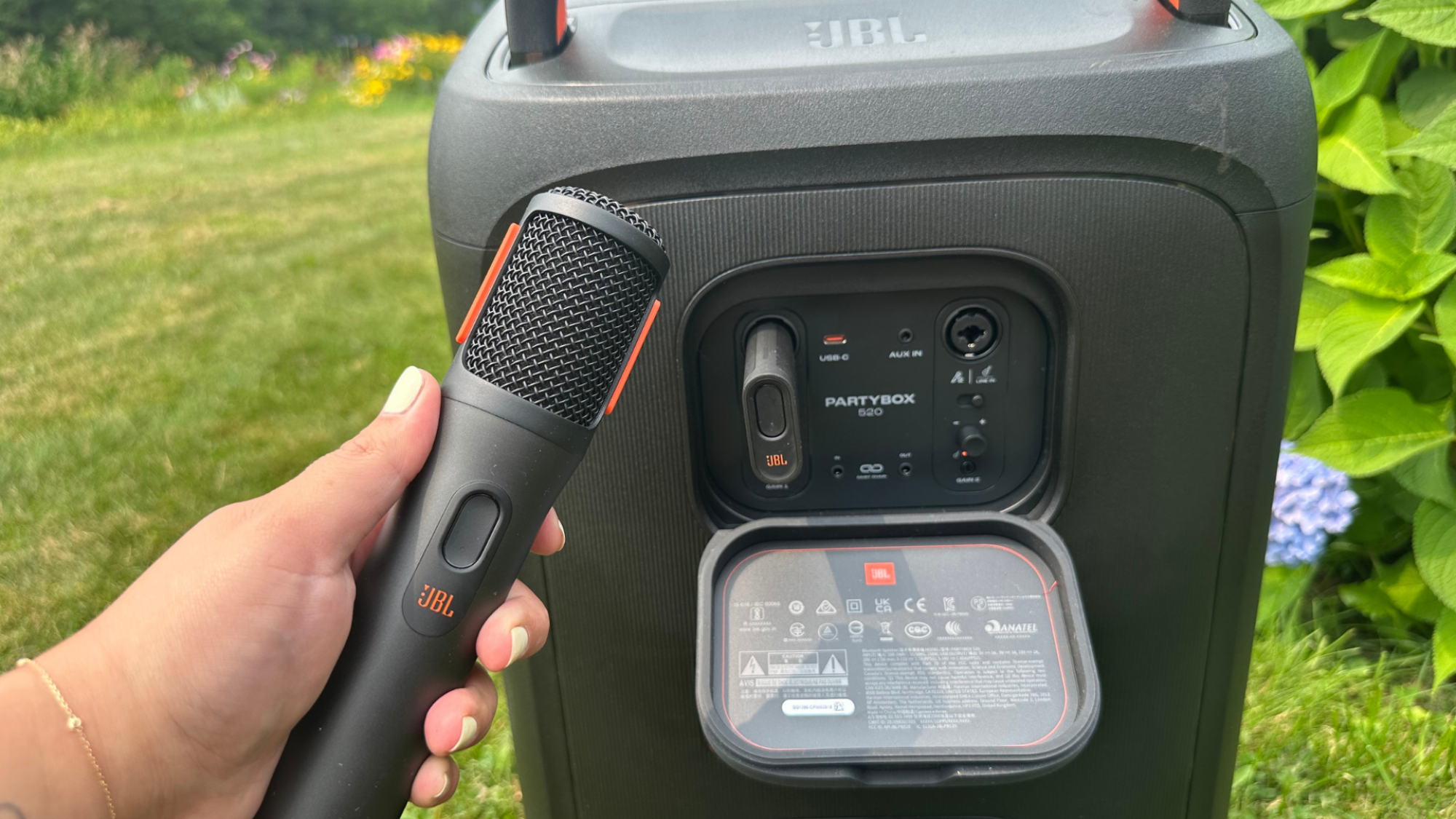 The rear side of the JBL PartyBox 520 and a hand holding up a wireless JBL microphone.