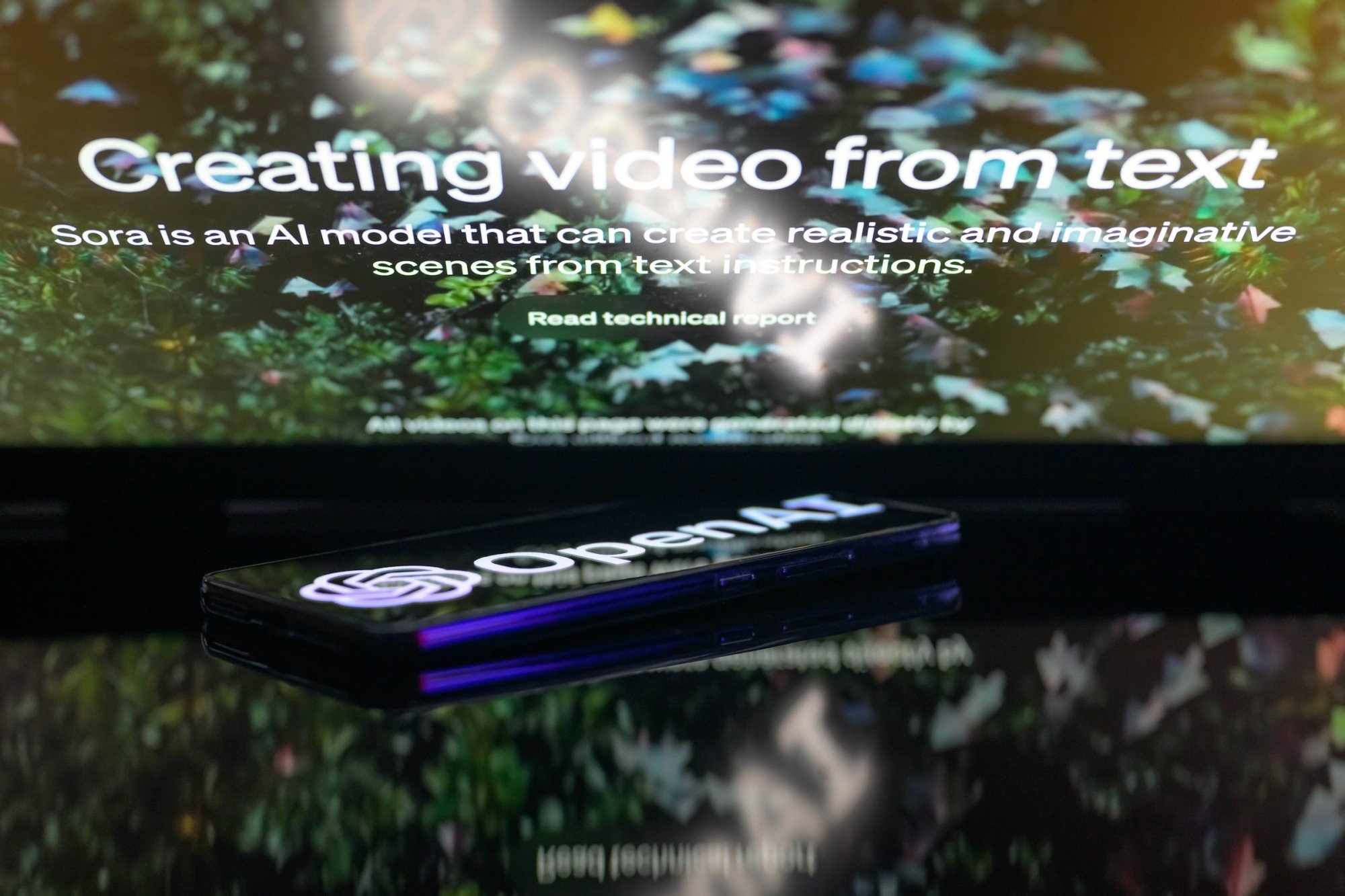 The OpenAI logo is being displayed on a smartphone with the Sora text-to-video generator visible in the background
