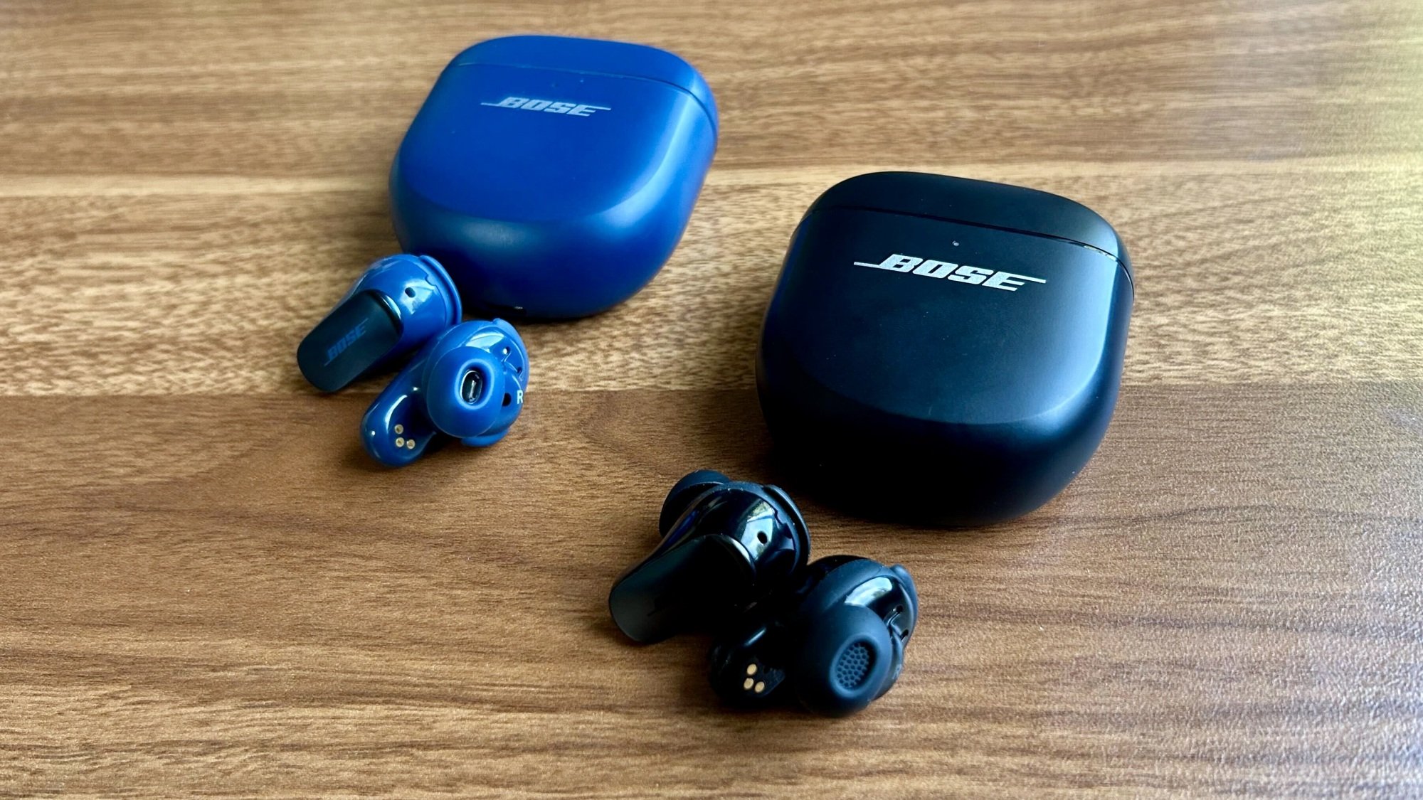 blue bose qc ultra earbuds on desk next to black second gen bose qc ultra earbuds