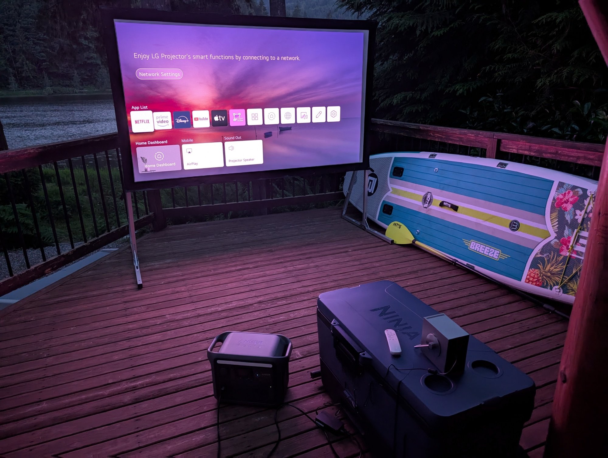 the anker solix c1000 portable power station connected to a projector in front a giant projector screen on a deck outside.