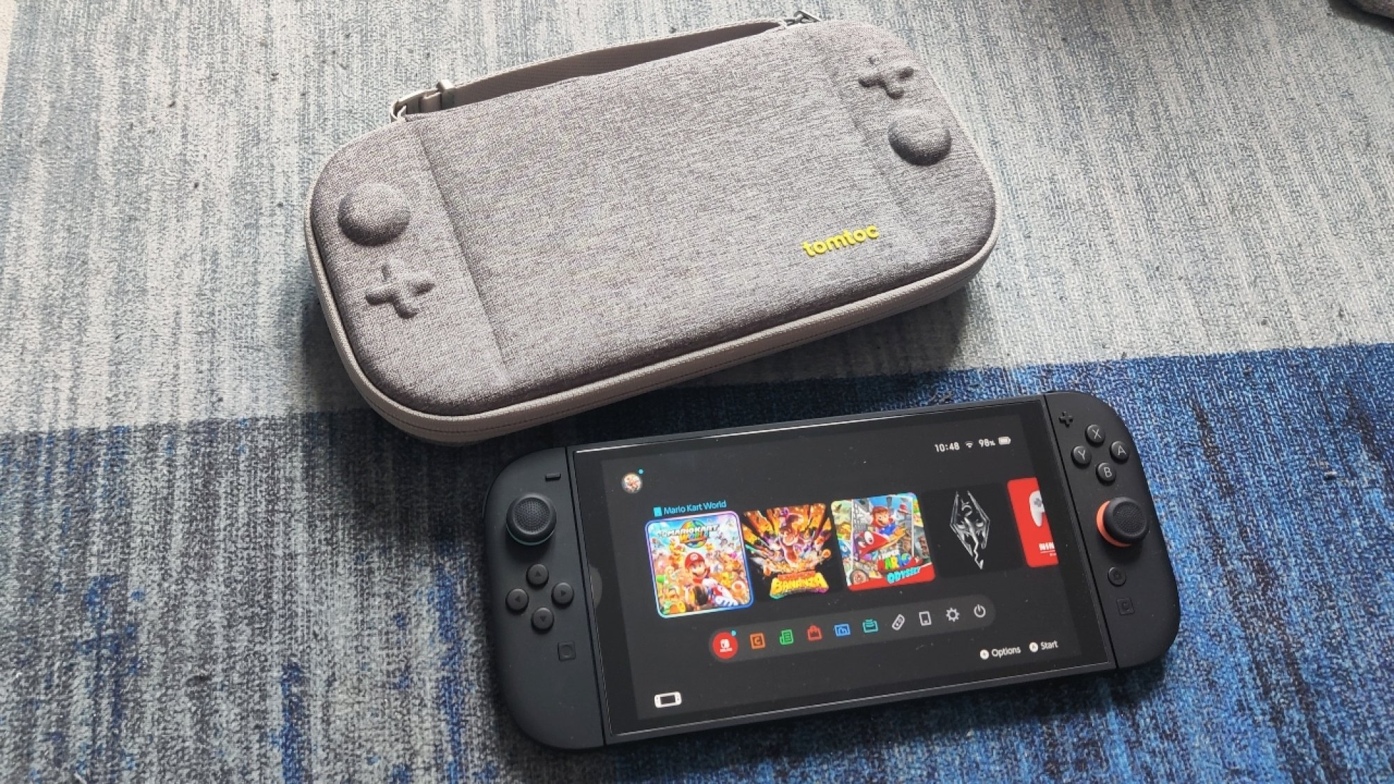 The tomtoc slim carrying case in grey above the Nintendo Switch 2, lying on a blue carpet
