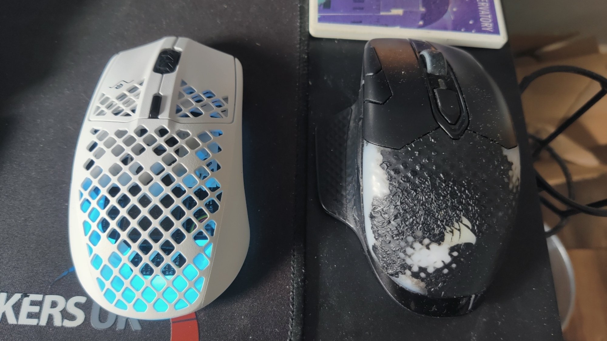 The SteelSeries Aerox 3 Wireless gaming mouse next to a worn Corsair Dark Core RGB Pro