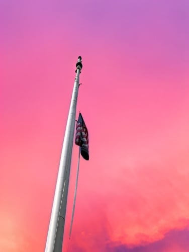 A flag pole in front of a very fake looking sunset
