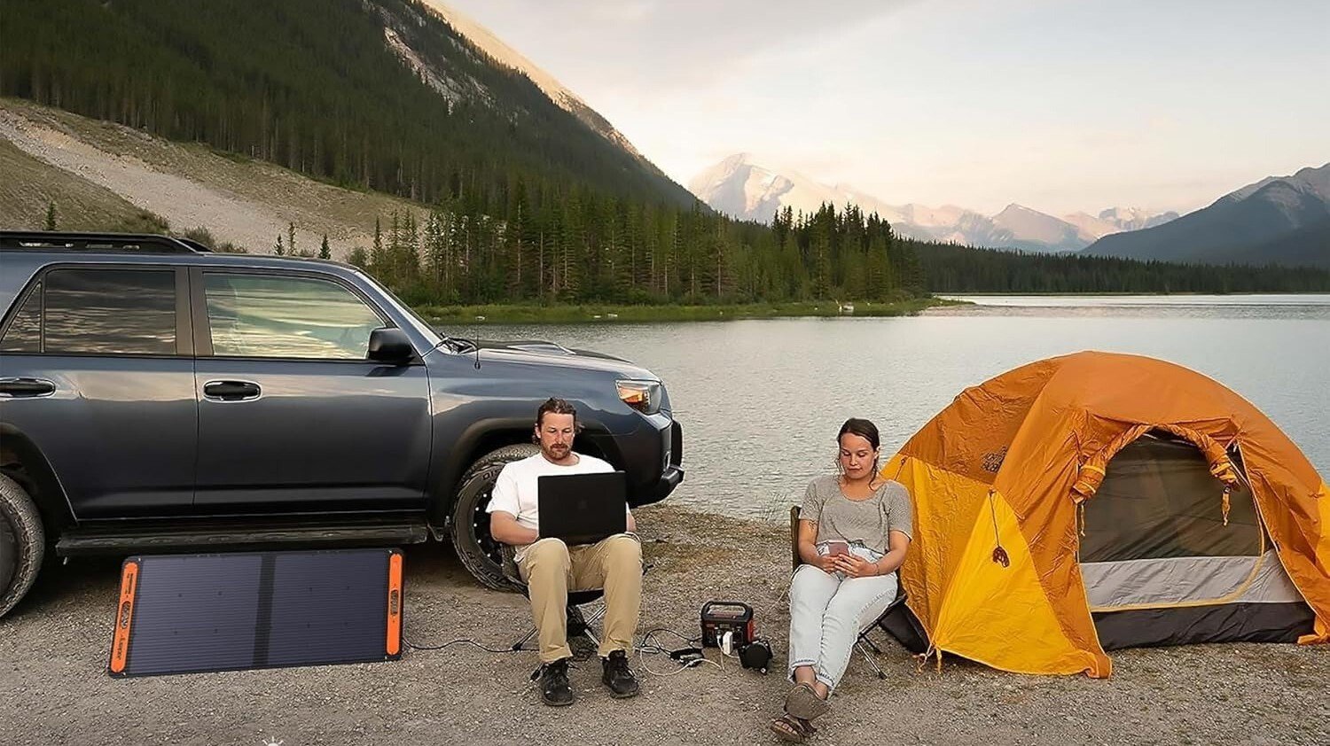two people sit outside next to a body of water while using electronics that are powered by the jackery e300 portable power station that's attached to a solar panel.