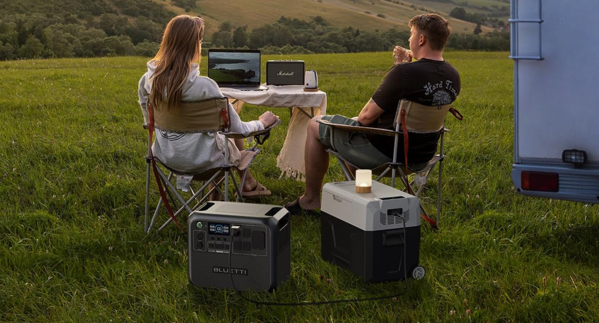 Two people at a campsite with their Bluetti solar generator sitting on the ground.